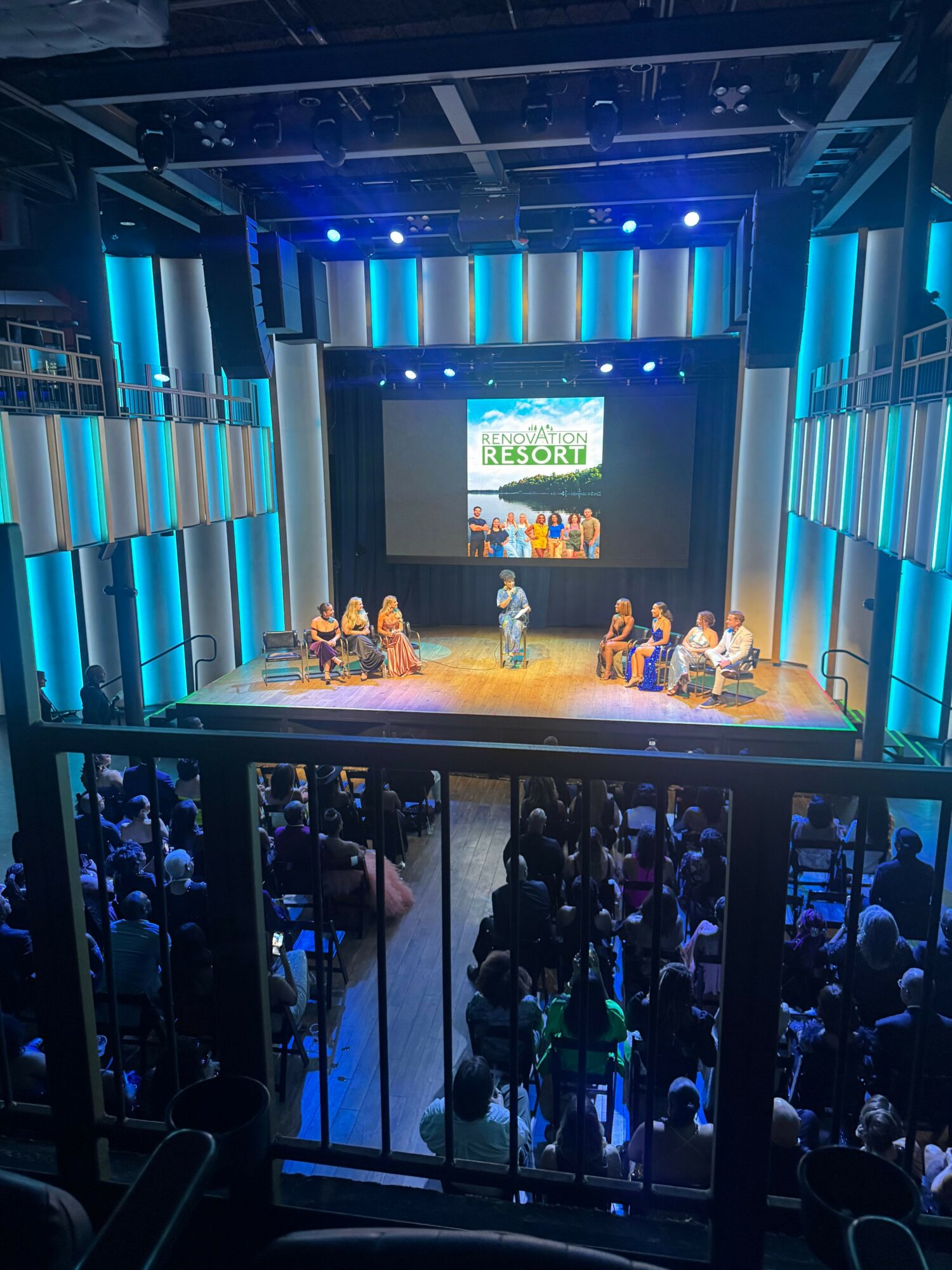 Stage with people, large screen, and audience in a theater or conference hall.
