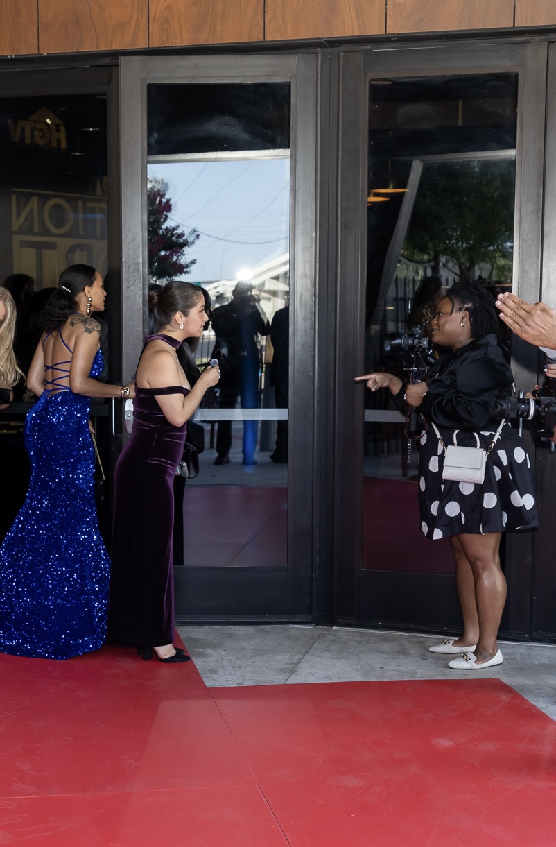 Group of women standing outside a glass door, some clapping, others talking, with reflections in the glass.
