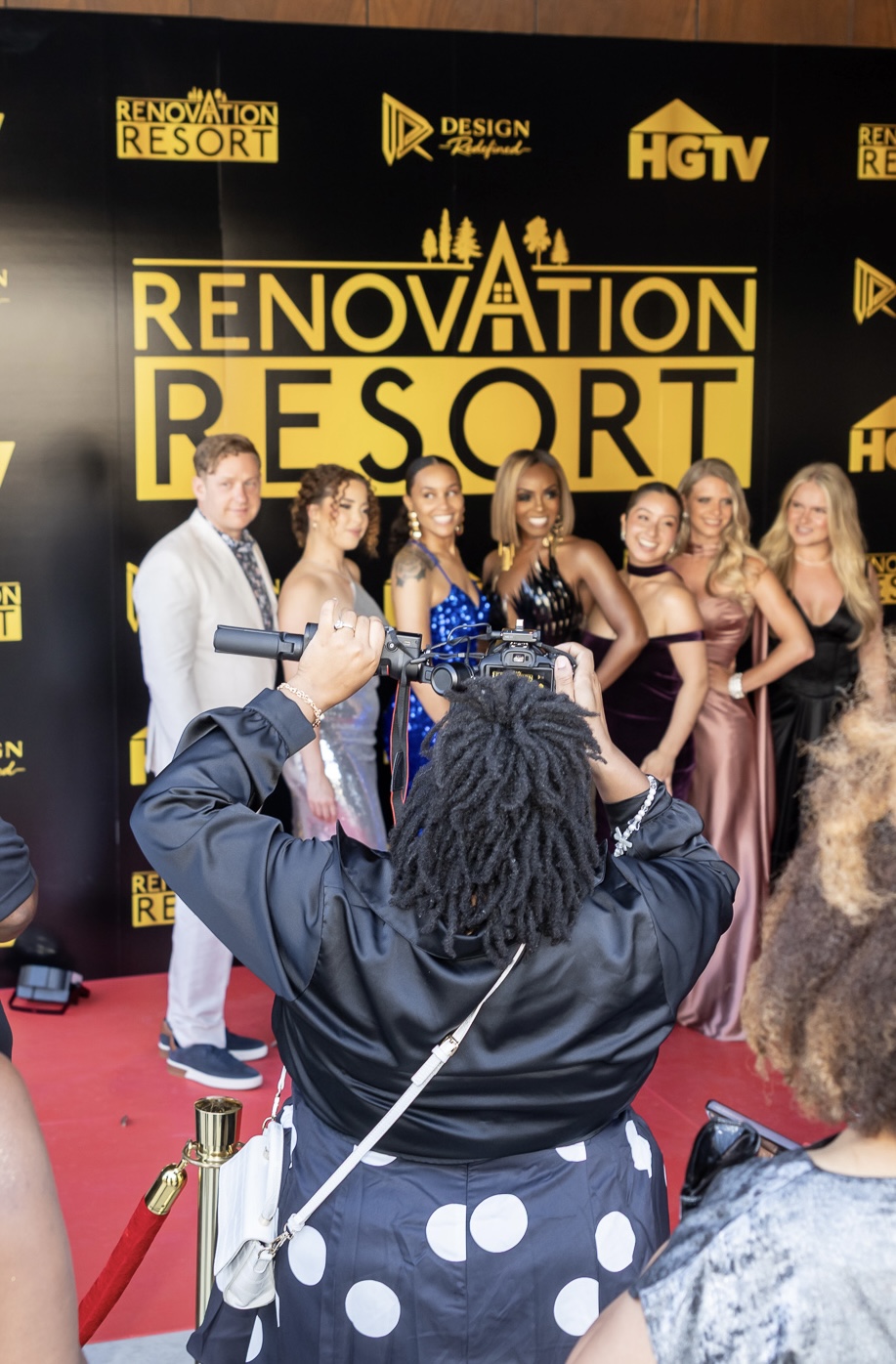 Group of women and one man posing on red carpet at Renovation Resort event, with a black backdrop displaying logos and text.
