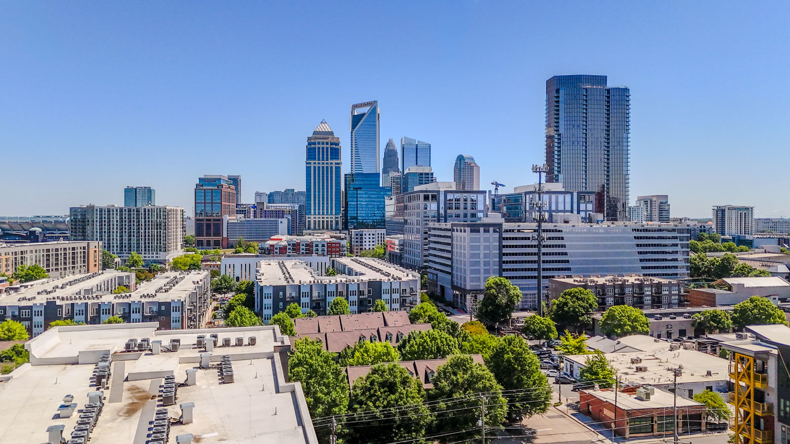 City skyline with tall buildings, trees, and clear blue sky.