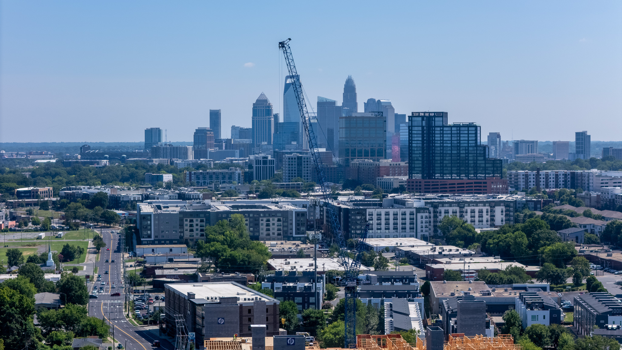 City skyline with tall buildings, construction crane, and a mix of modern and older structures under a clear blue sky.