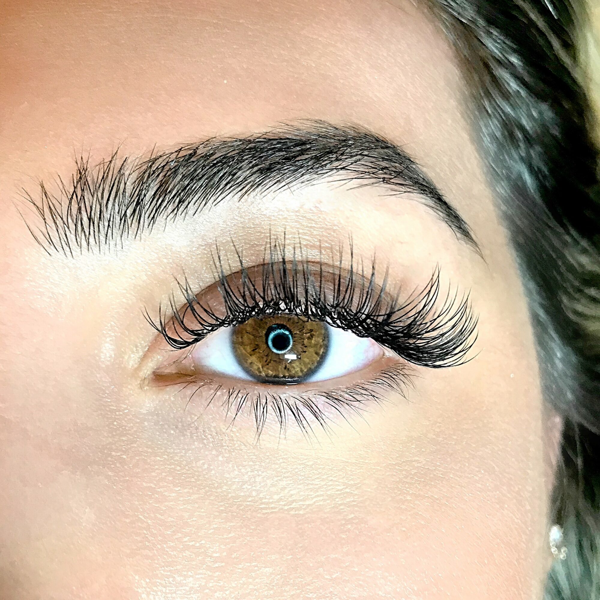 Close-up of a person's eye with brown iris, long eyelashes, and well-groomed eyebrow, looking slightly upward.