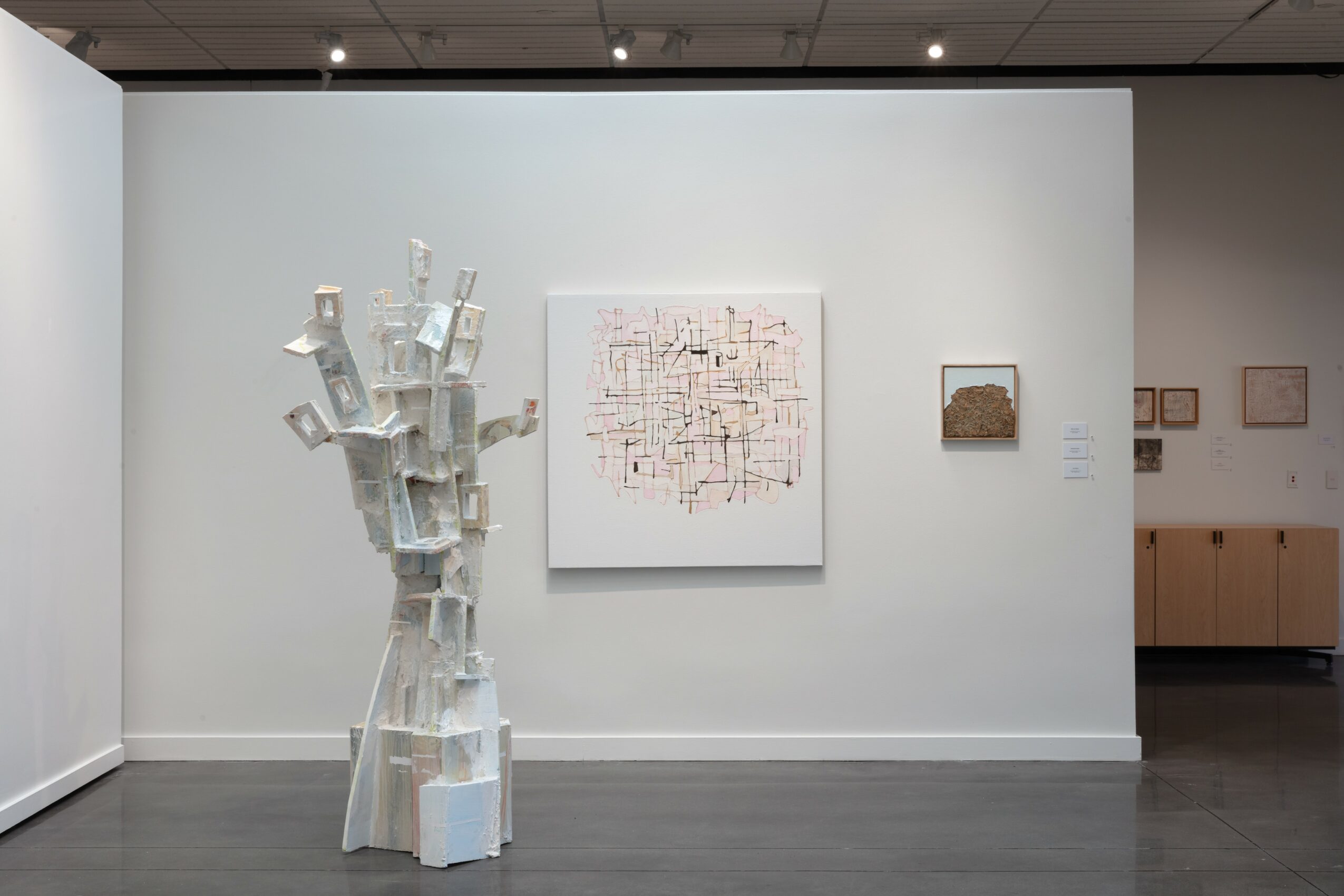 Gallery wall with abstract artwork, sculpture, and small framed pieces, in a modern art exhibition space.