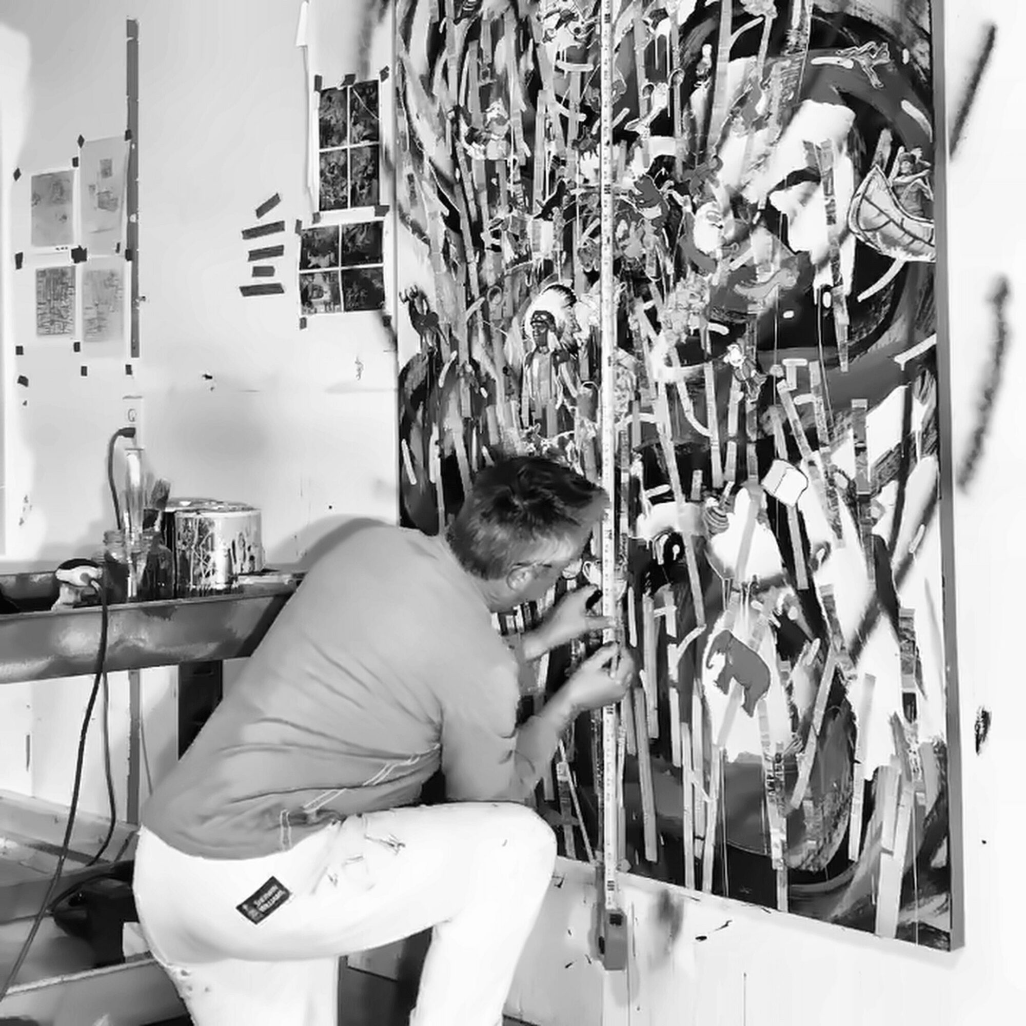 Person working on a large abstract painting in an art studio, with photos on the wall behind.