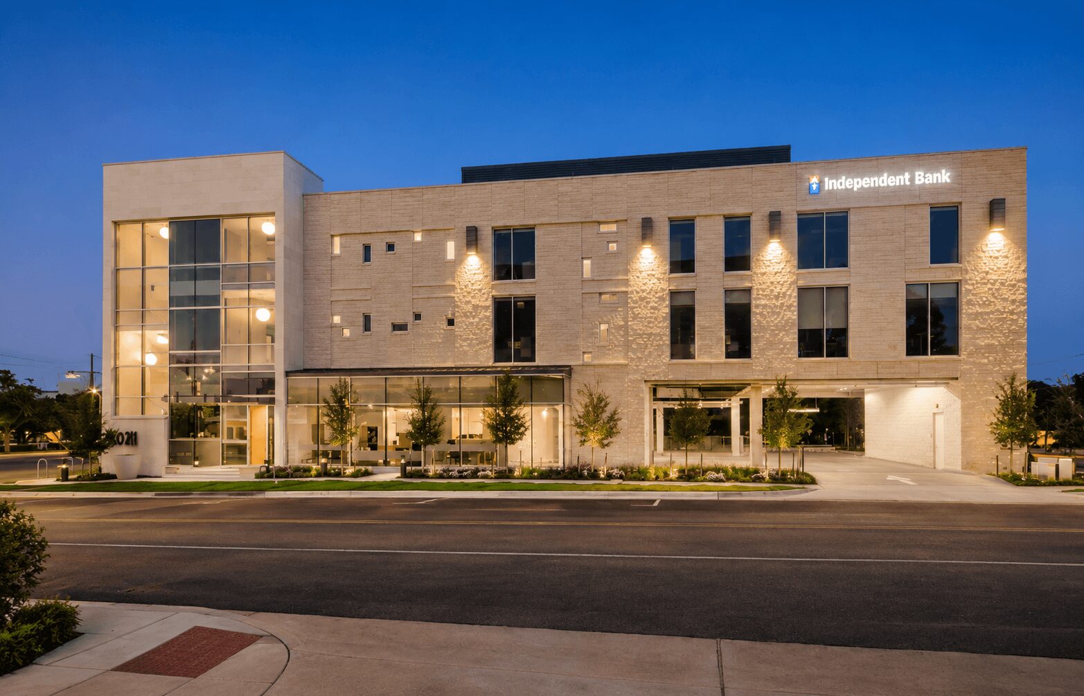 Modern bank building with illuminated windows and trees in front, under a clear evening sky.