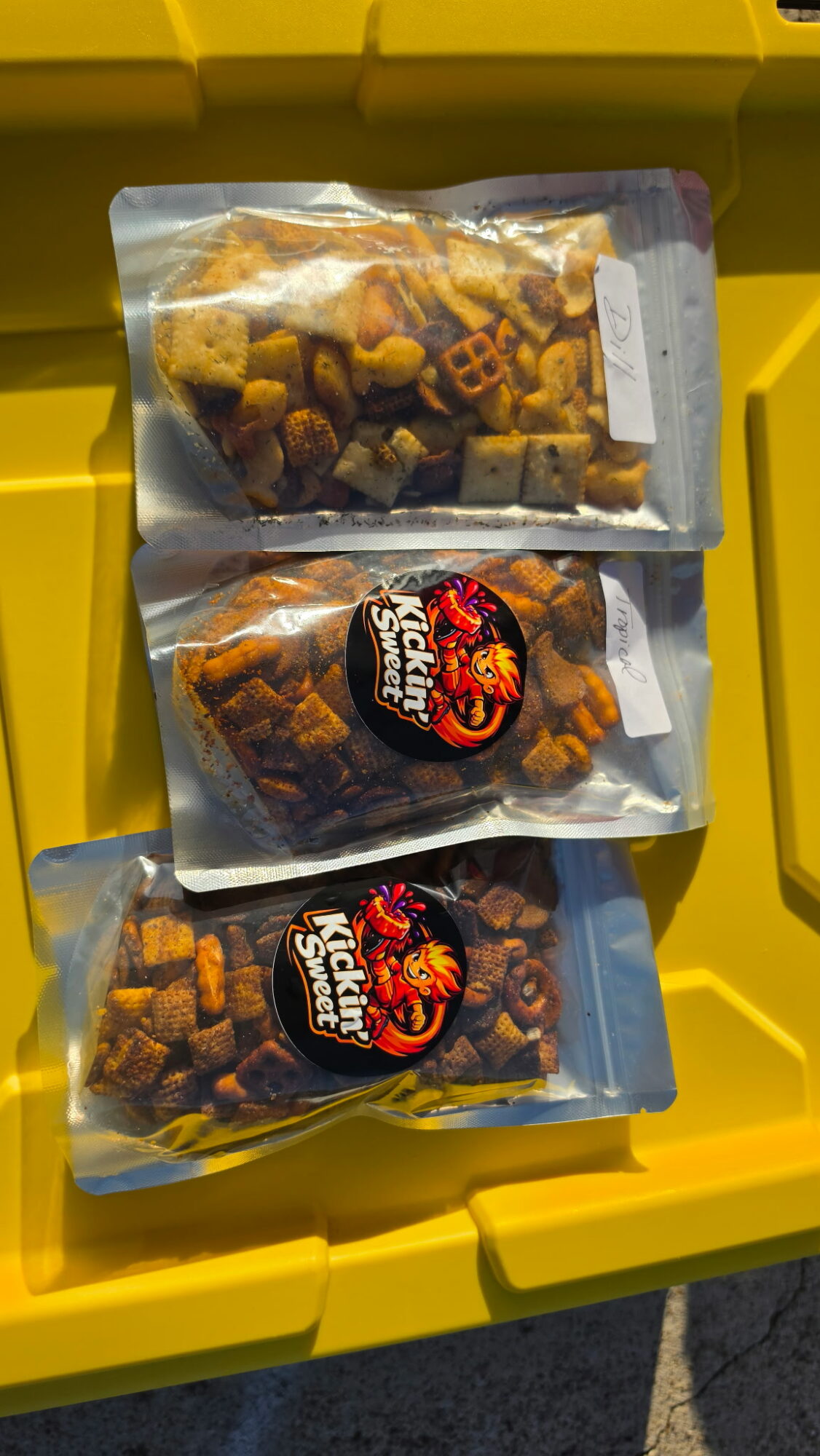 Three plastic bags of snack food with colorful labels, placed inside a yellow container.