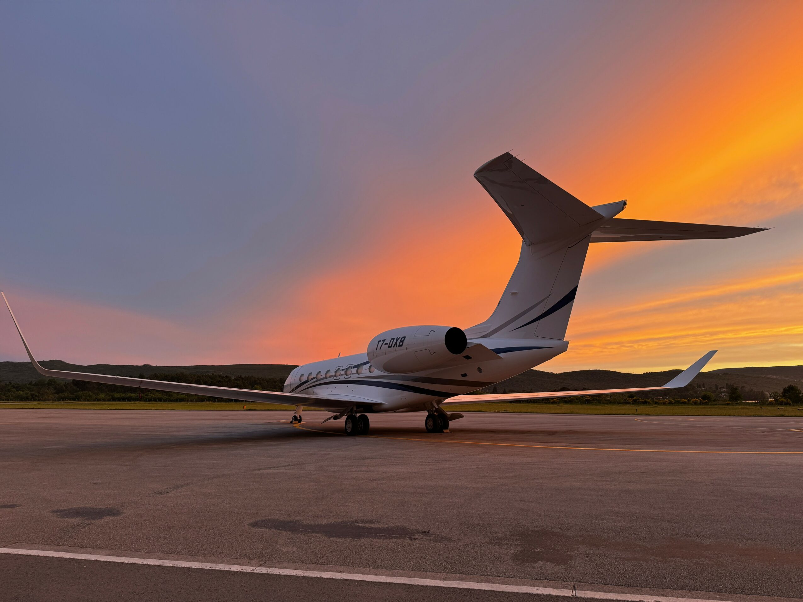 Private jet parked on runway during sunset with colorful sky and horizon in background.
