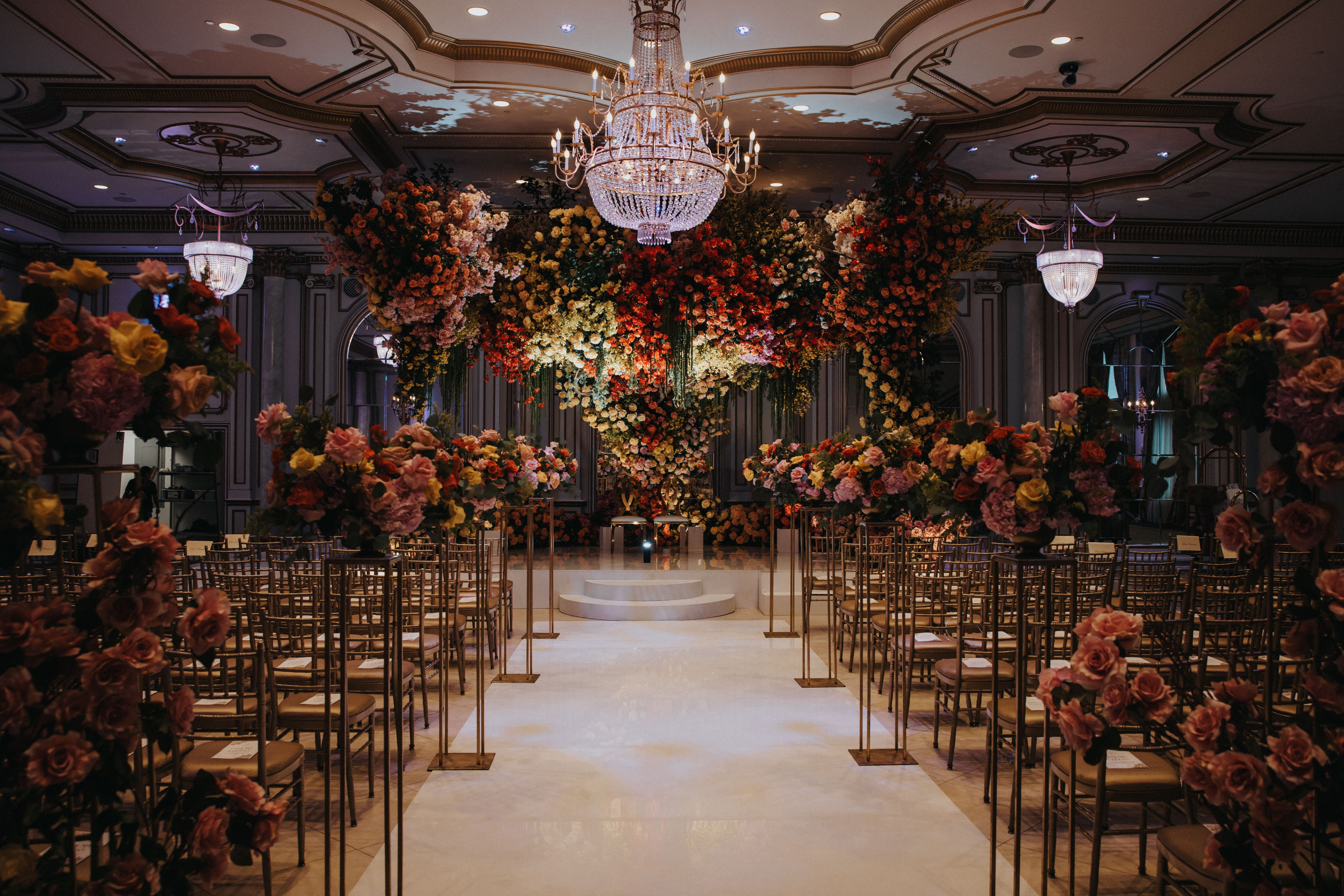 Elegant event hall with a chandelier, floral arrangements, and rows of chairs, ready for a ceremony or celebration.