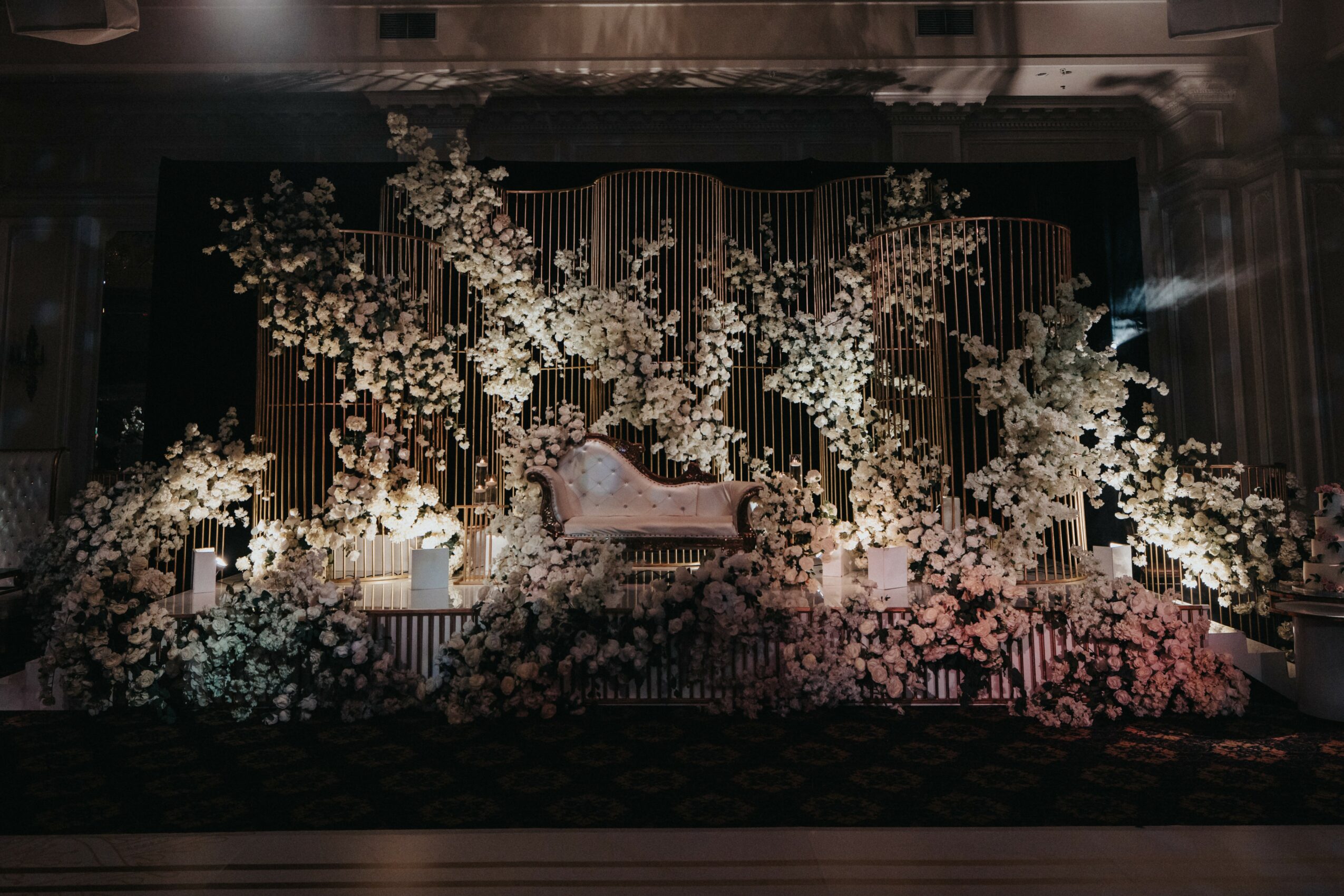 Elegant stage with floral arrangements and a central ornate sofa, decorated with white flowers and gold accents.