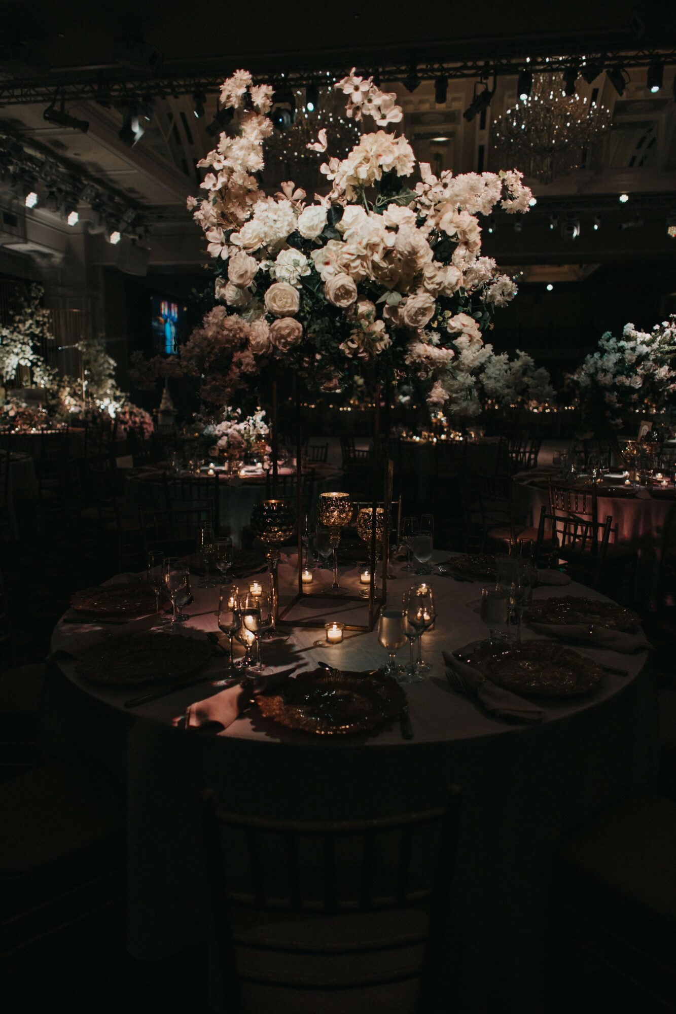 Elegant event table with floral centerpiece and candles, dimly lit with chandeliers overhead.