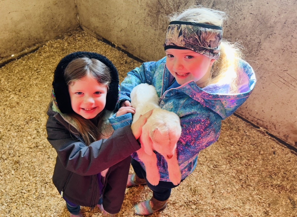 Two children holding a small animal inside a concrete enclosure, smiling and looking at the camera.