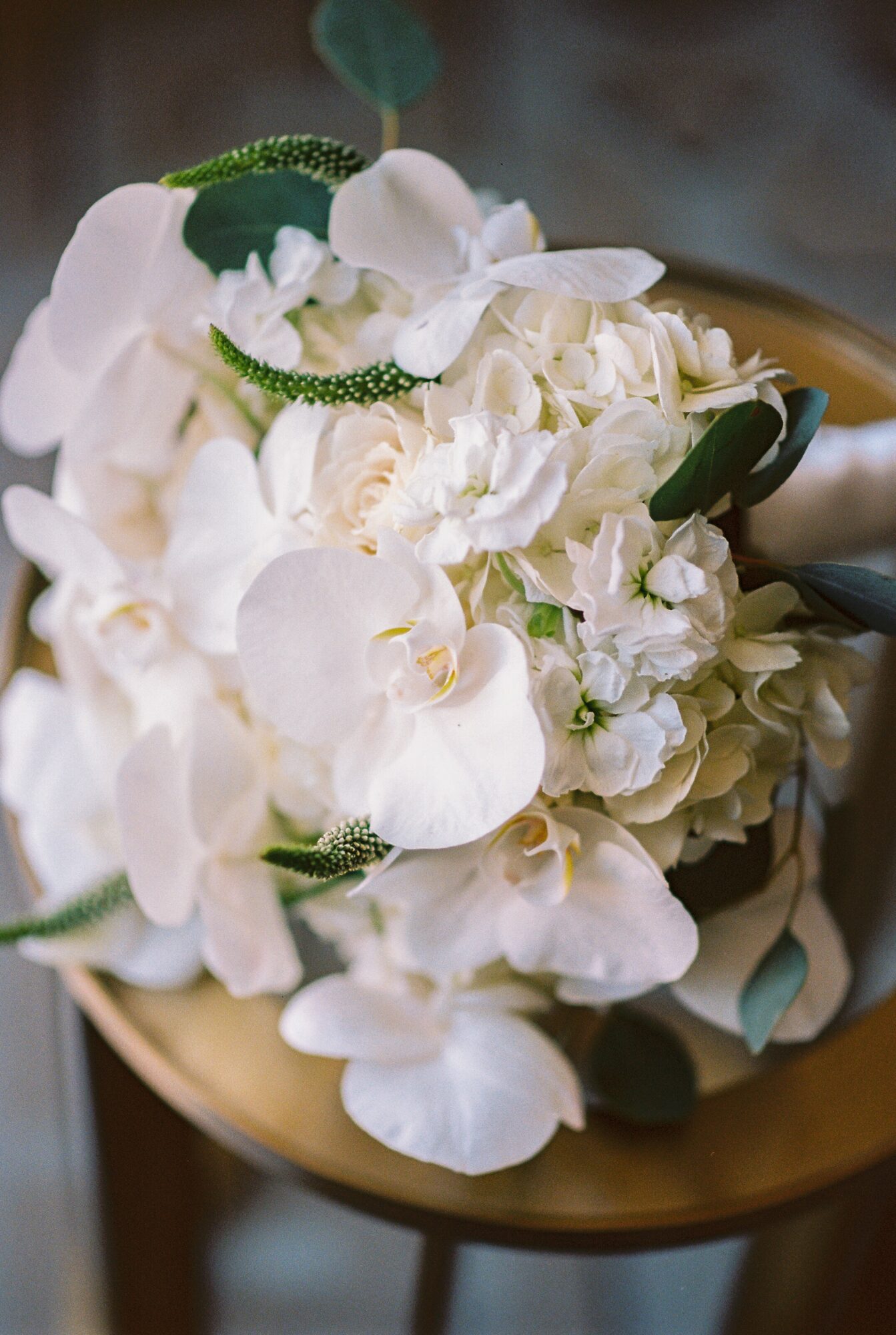 Close-up of a white floral bouquet with orchids and greenery on a gold plate.