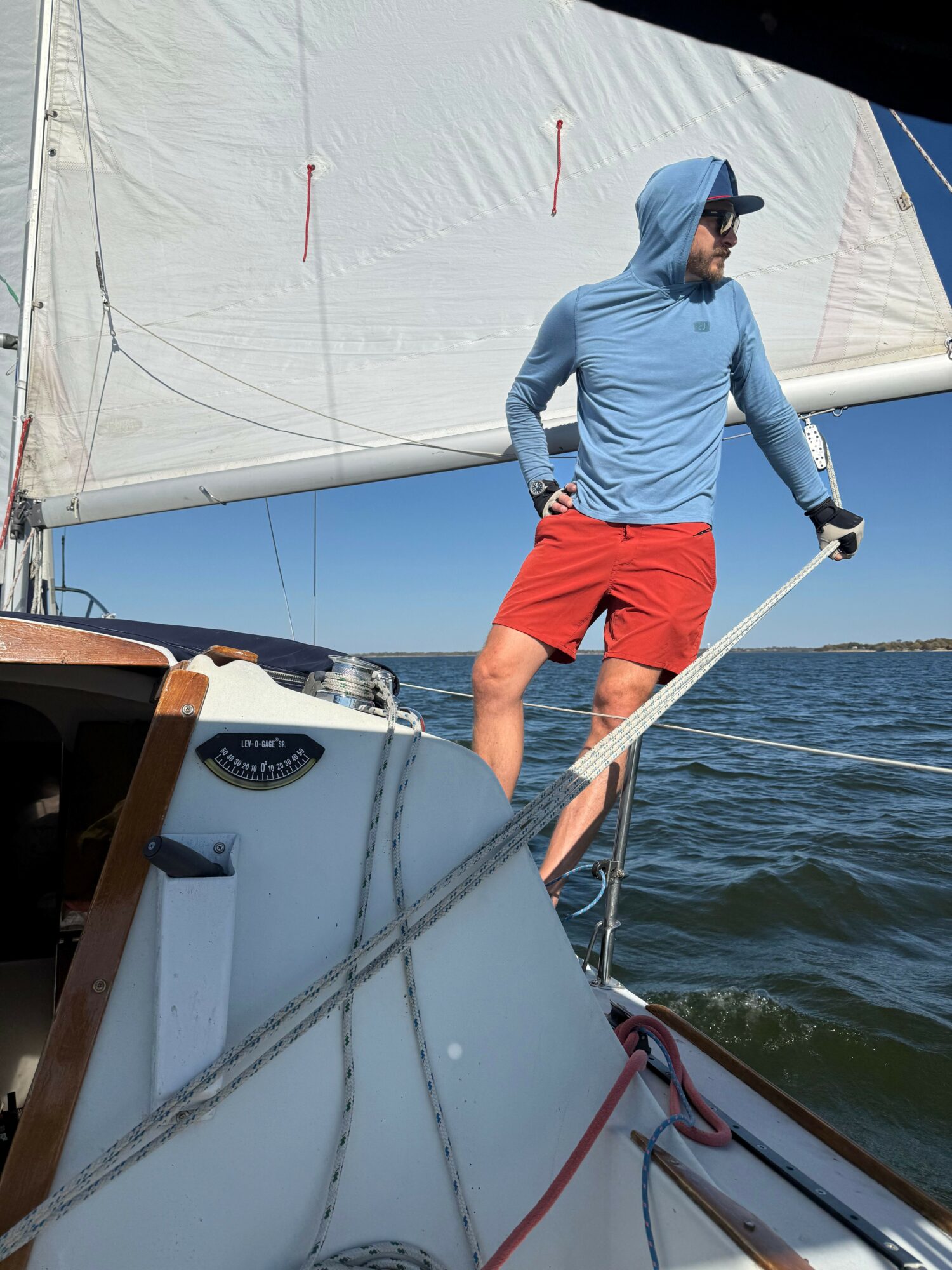 Person standing on a sailboat deck holding a rope, with water and sky in the background.