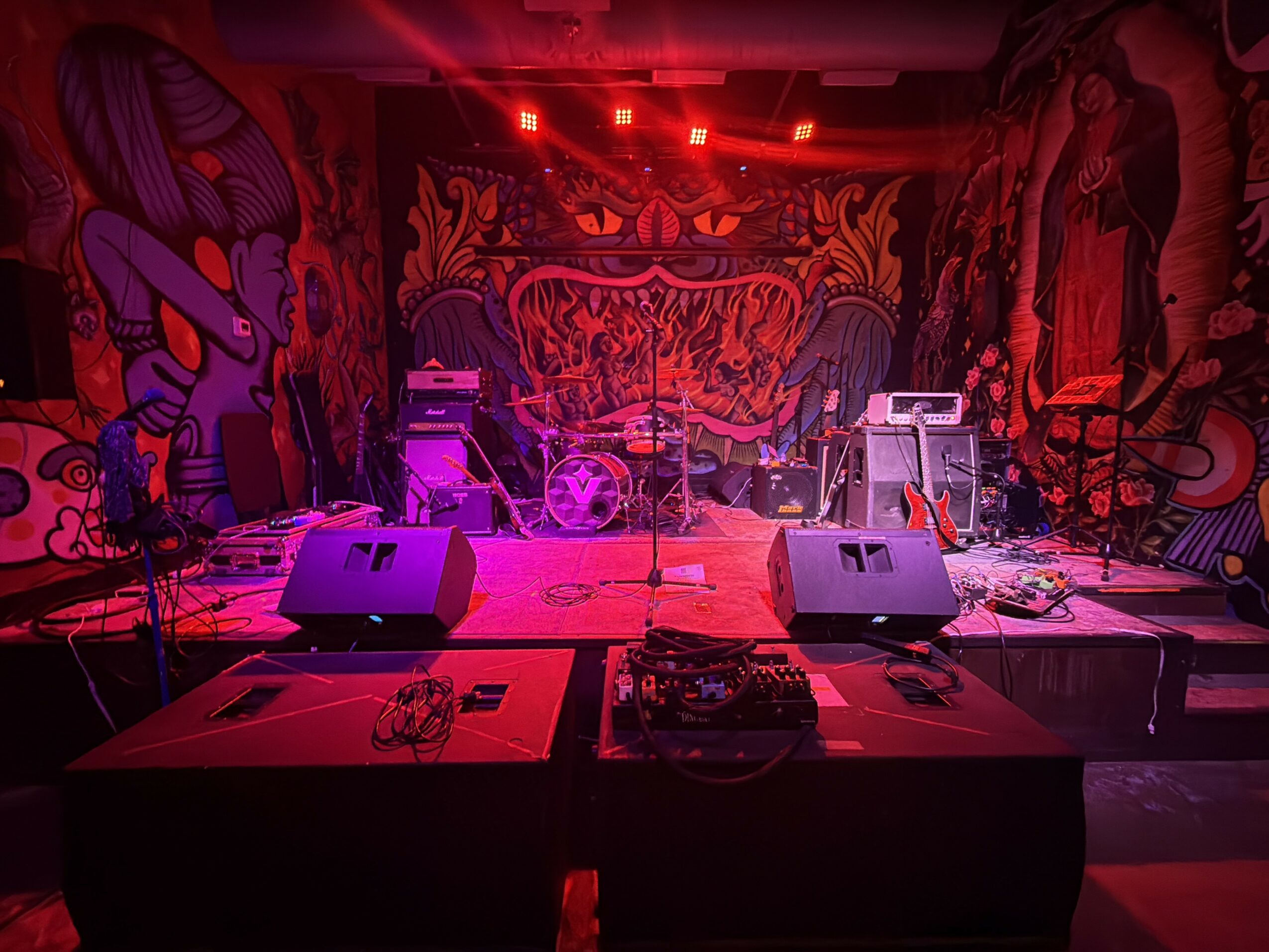 Stage with musical instruments and equipment, colorful graffiti-style murals in background, red lighting, ready for a performance.