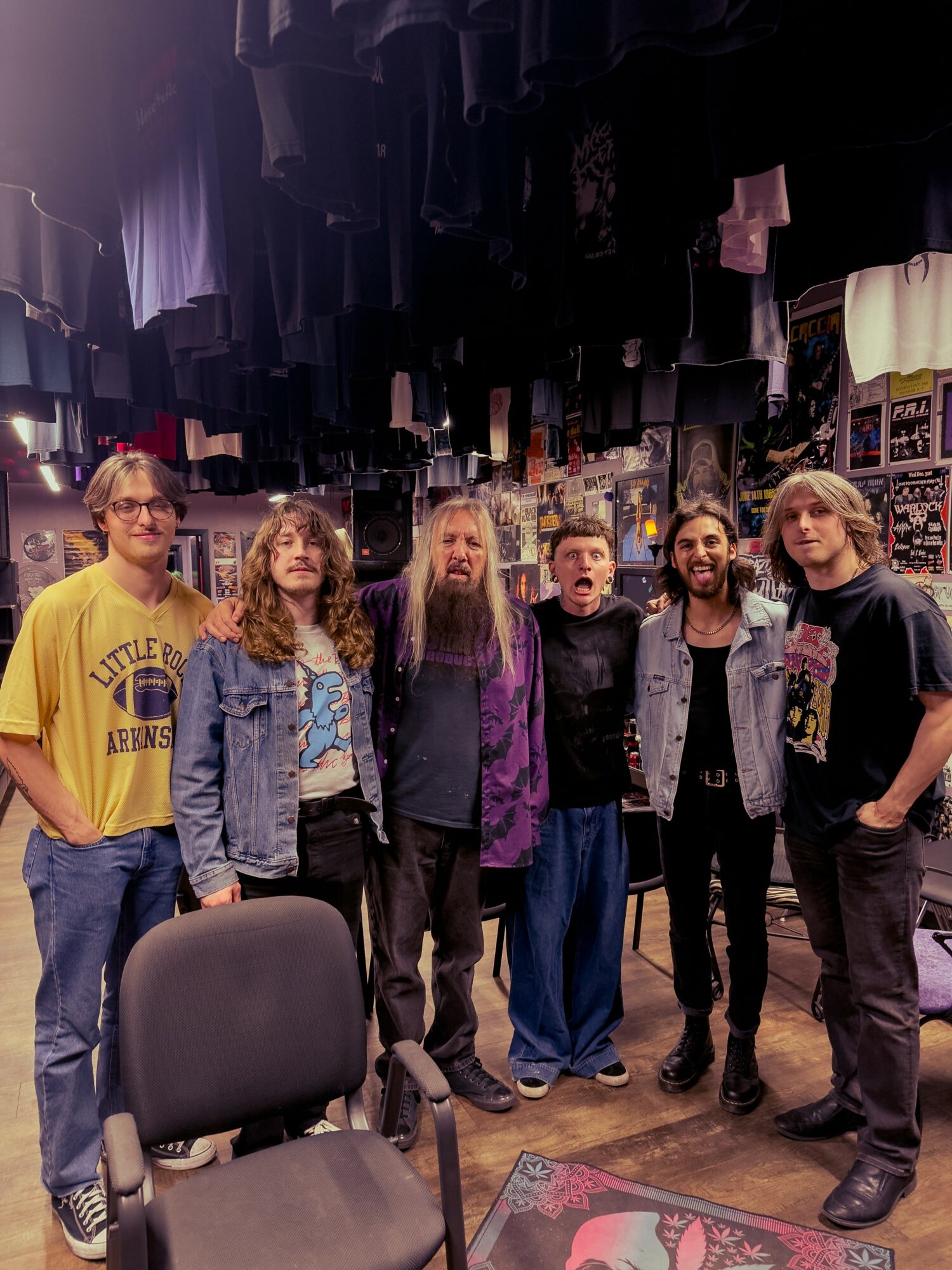 Six people standing together in a clothing store with hanging clothes above them, smiling and posing for the photo.