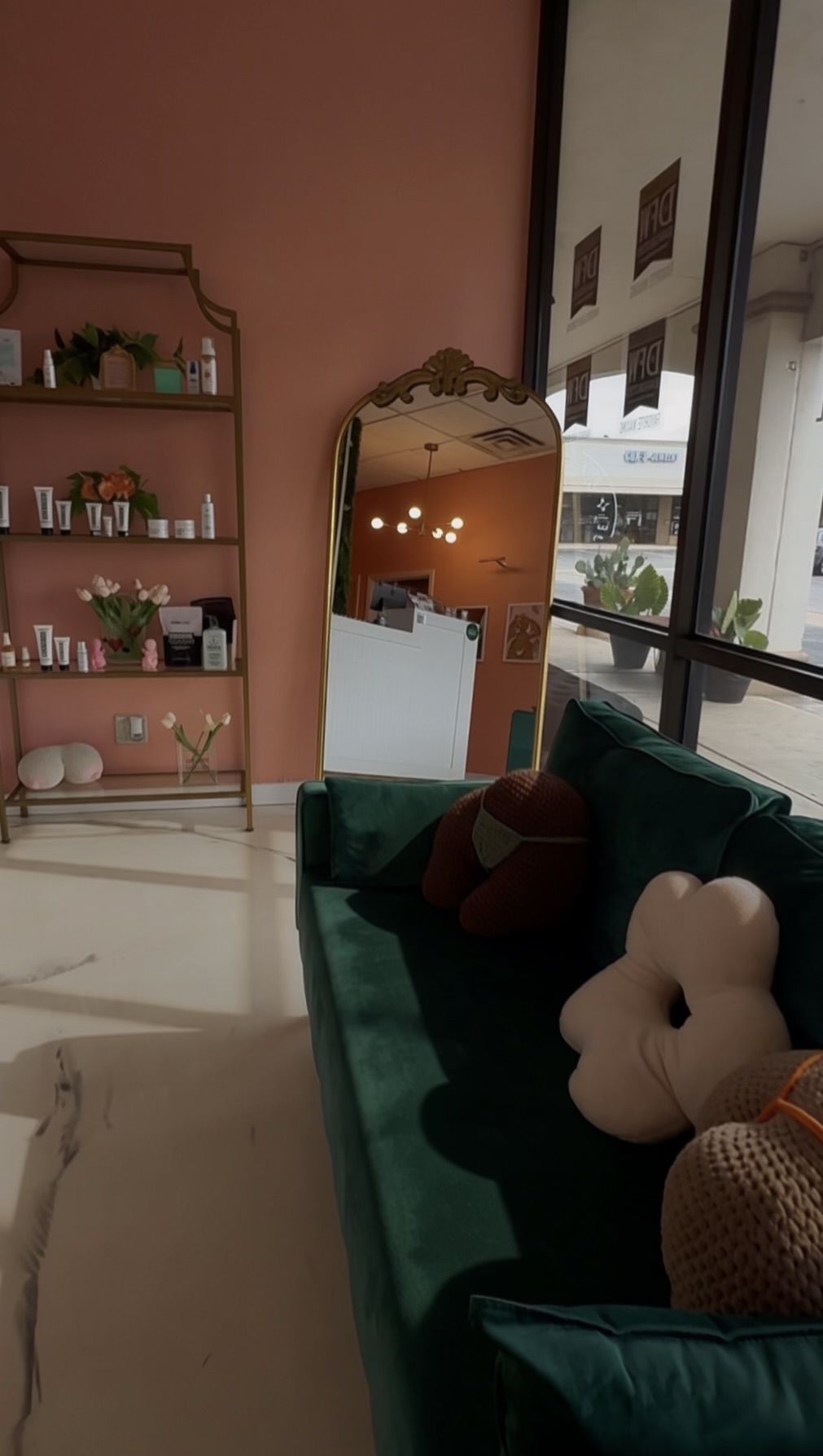 Living room with pink wall, green sofa, decorative pillows, and a tall mirror reflecting lights and window.