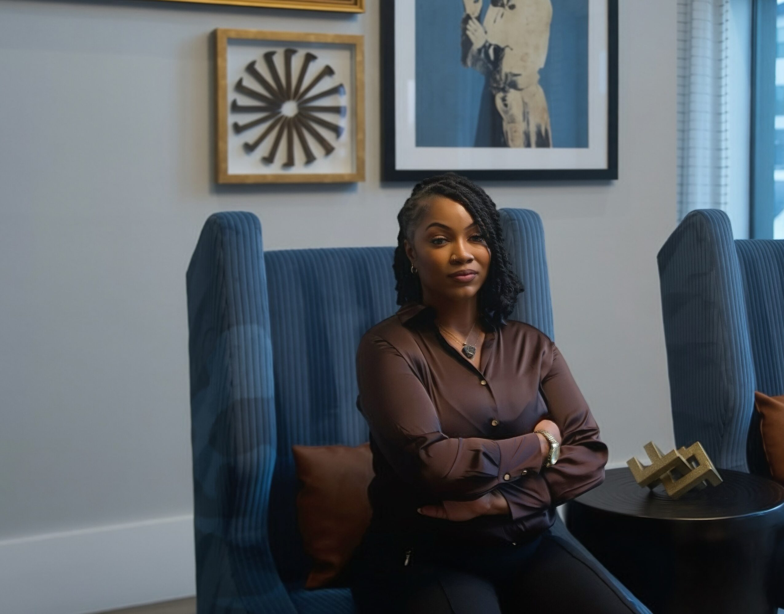 Woman sitting in a blue chair with artwork on the wall behind her.