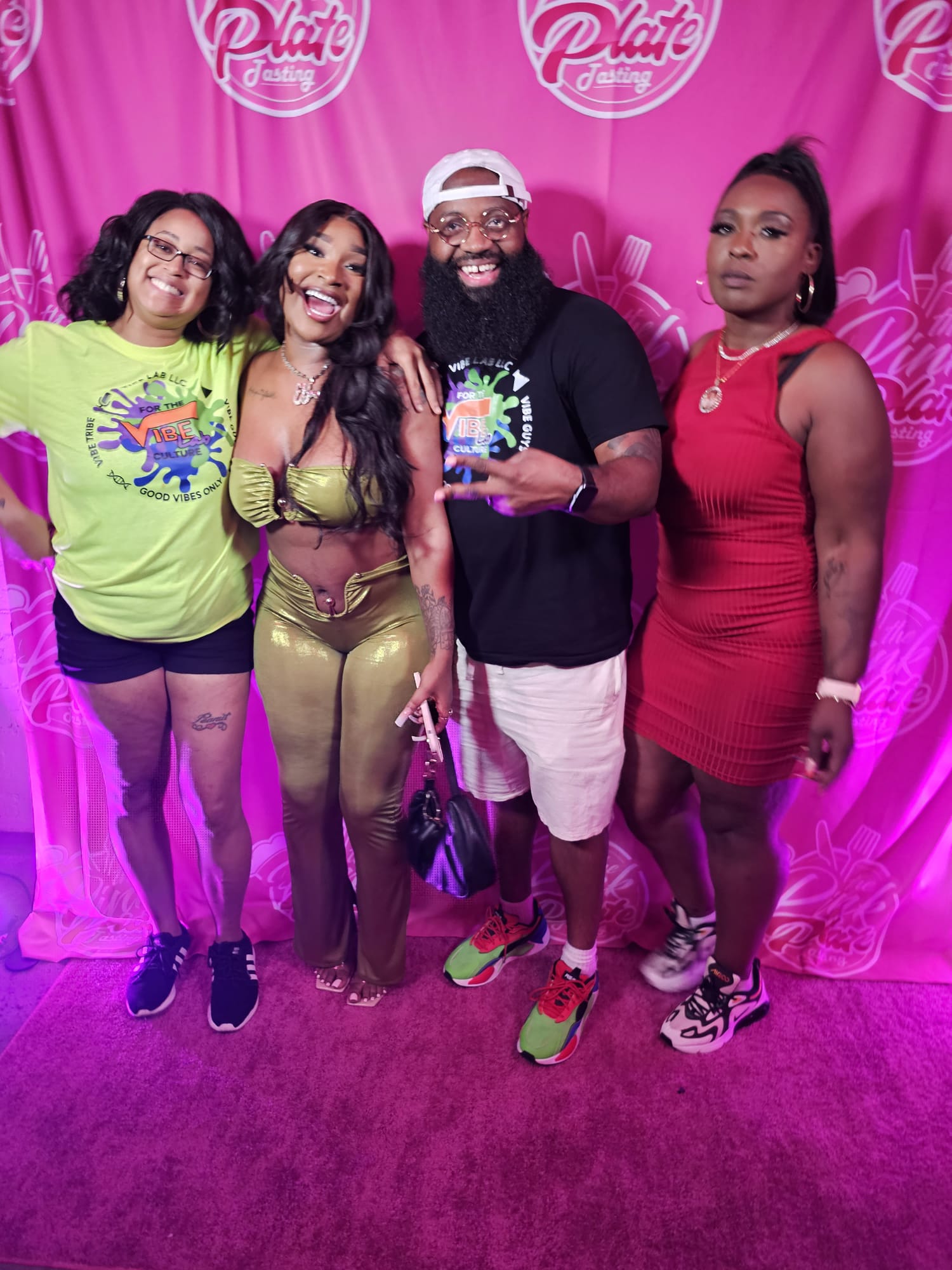 Four people standing together in front of a pink backdrop with logos, smiling and posing for the photo.