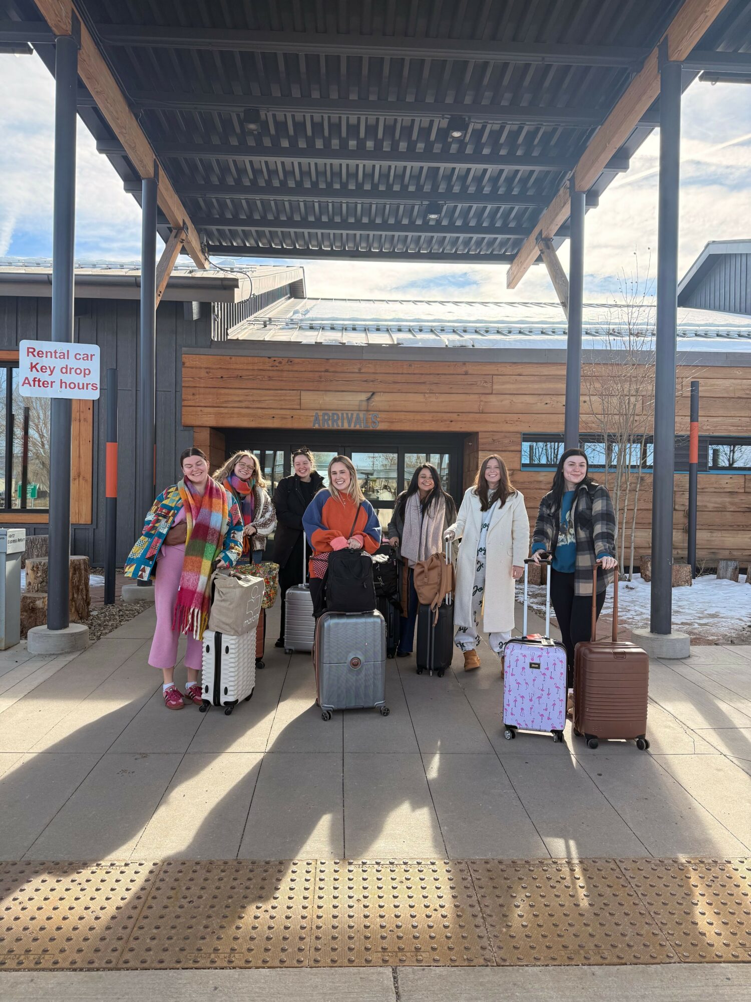 Group of people with luggage standing on a platform under a roof, with a train in the background.