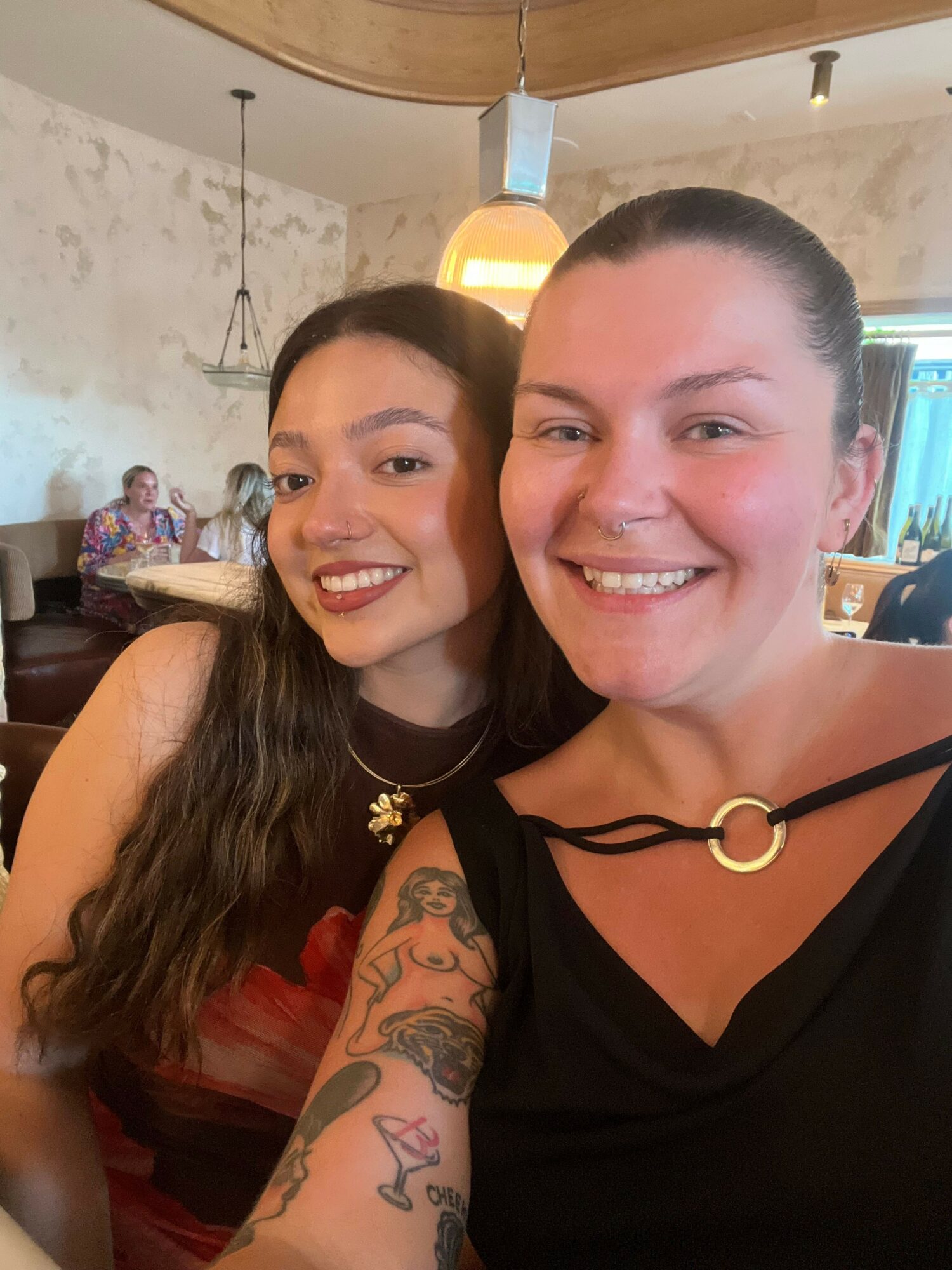 Two women smiling, one with dark hair and the other with light hair, in an indoor setting.