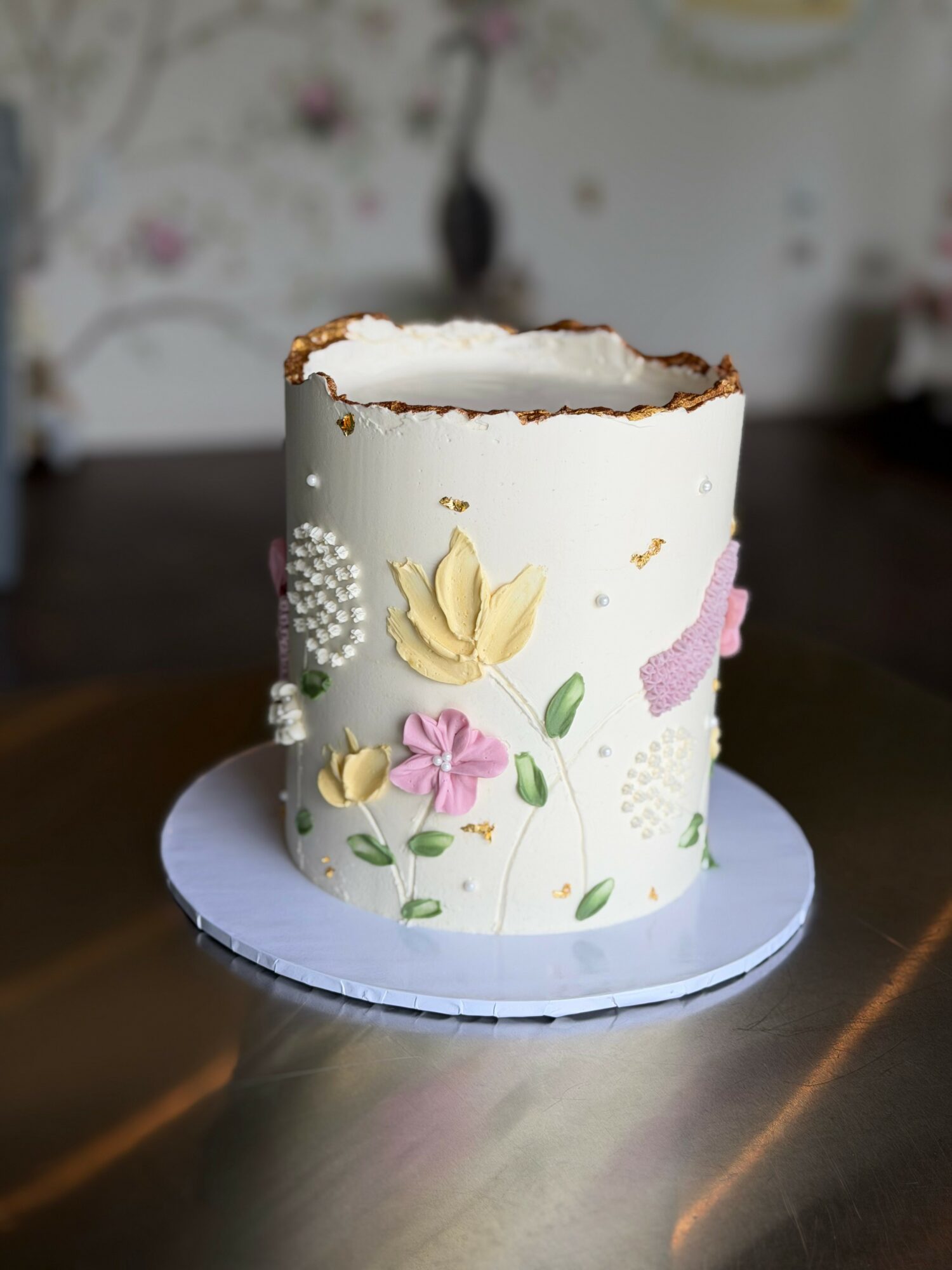 A partially eaten white cake with floral decorations on a white base, placed on a dark surface.