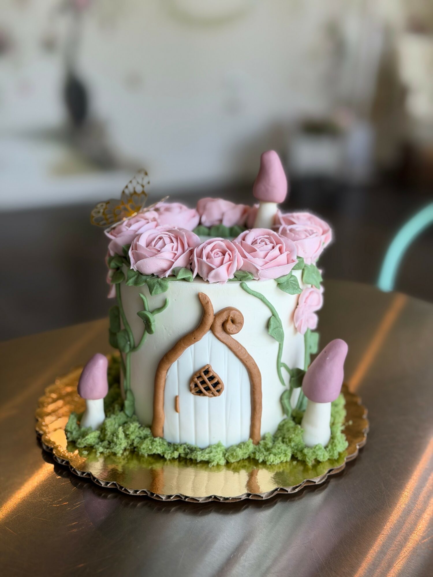Decorative cake with pink roses, a birdhouse door, and pink and white cone-shaped decorations, on a gold base.