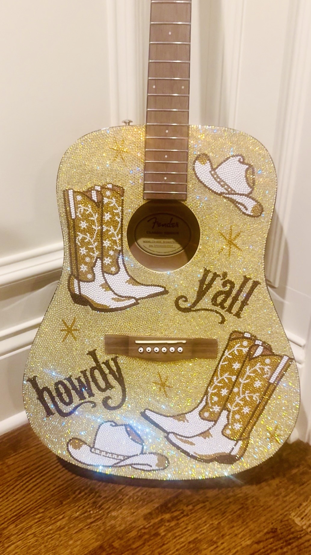 Decorated guitar with cowboy boots, hat, and stars, featuring the words 