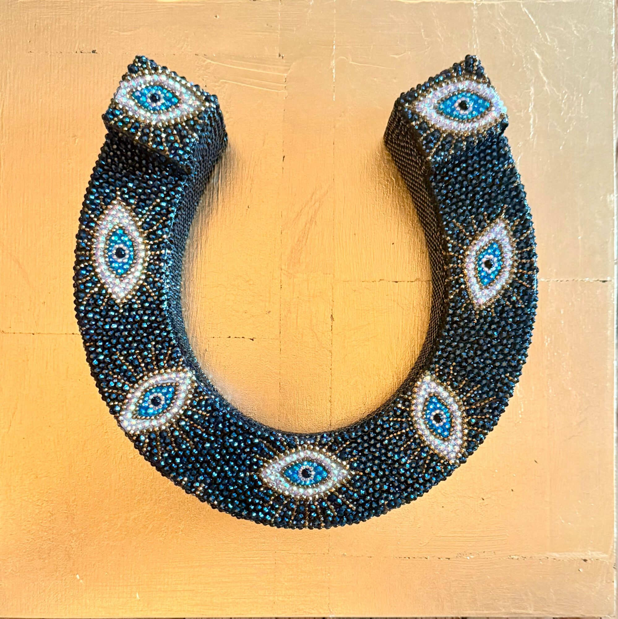 Beaded necklace with eye patterns, curved shape, on a beige surface.