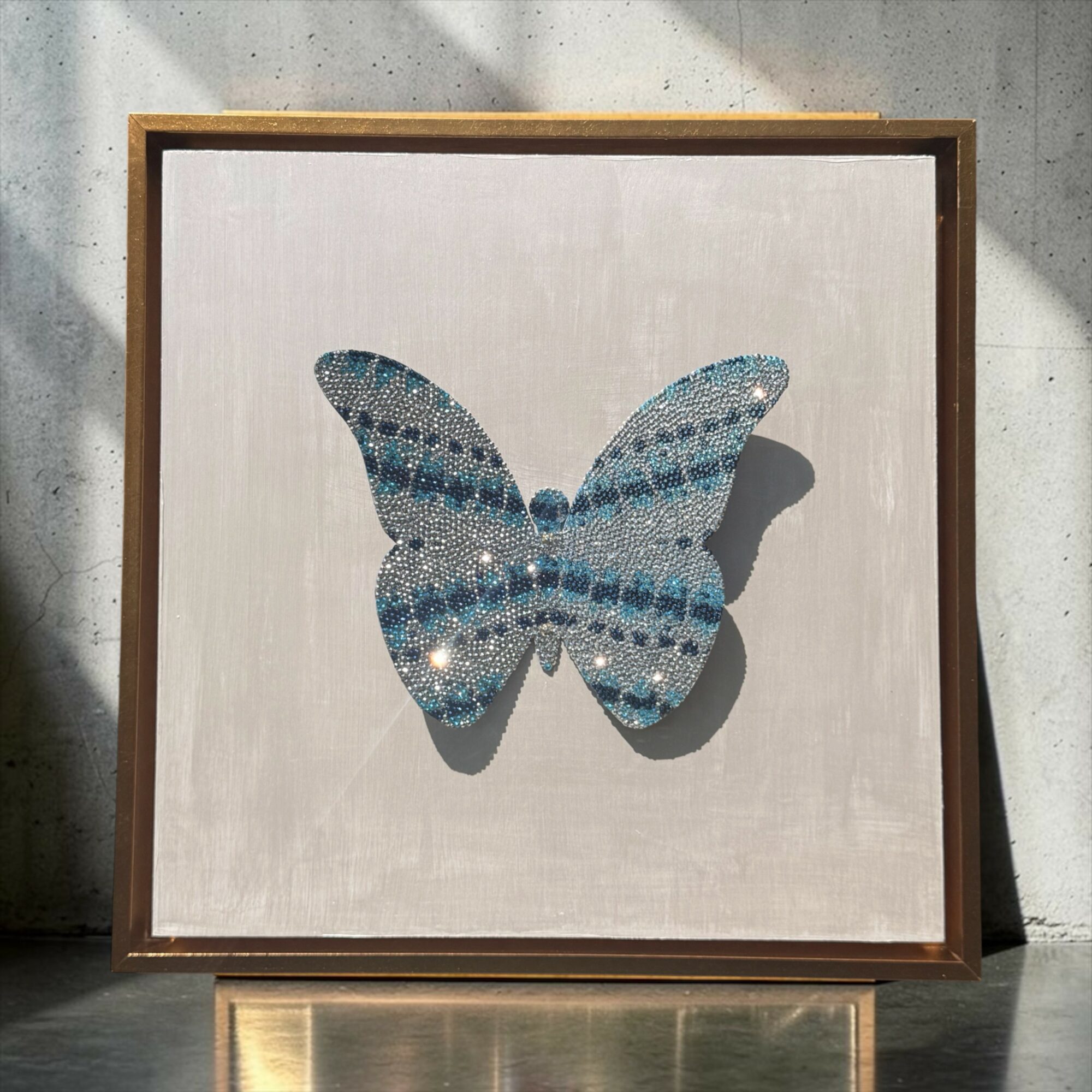 Framed artwork of a butterfly with blue and white patterns, shadow cast on a light-colored background.