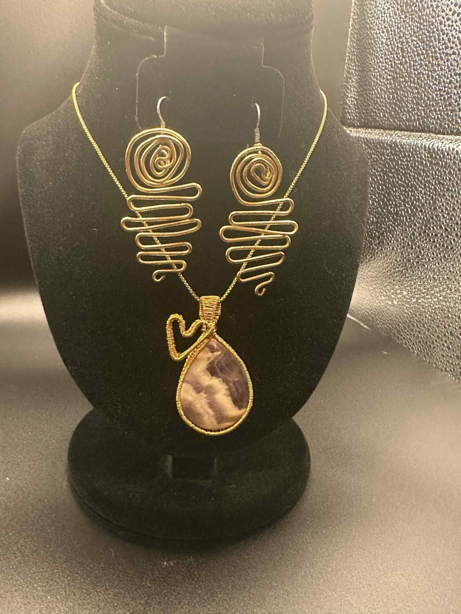 Decorative necklace with spiral and wave designs on a black bust, with a large oval pendant, against a plain background.