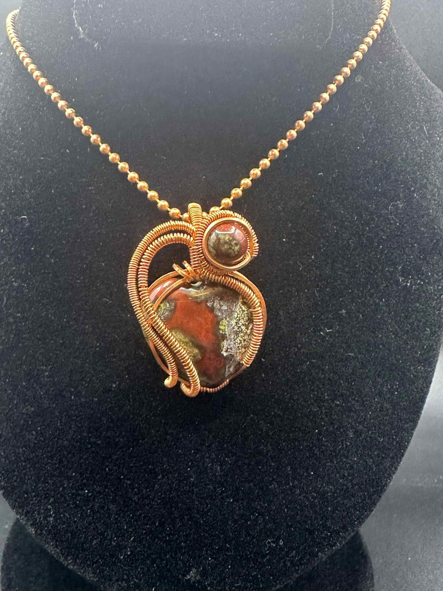 Gold necklace with a large, oval, multicolored gemstone pendant on black background.