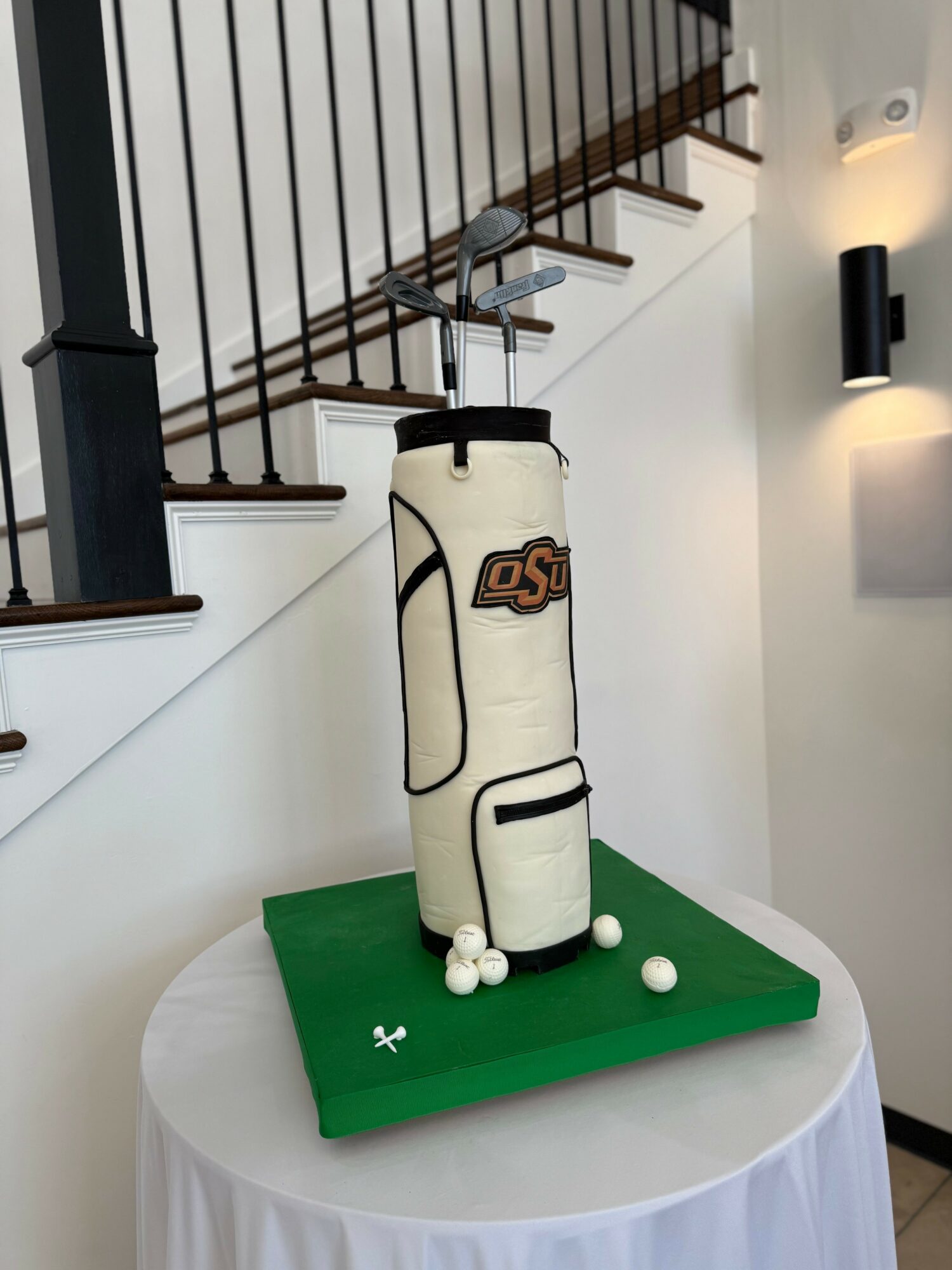 Golf bag-shaped object on a table with golf balls, in a room with staircase and wall light, neutral colors.
