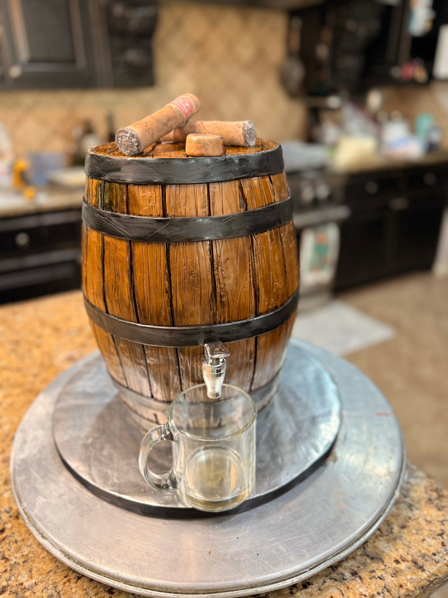 Barrel-shaped container with cigars on top, a spigot, and a glass mug underneath, placed on a round metal tray.