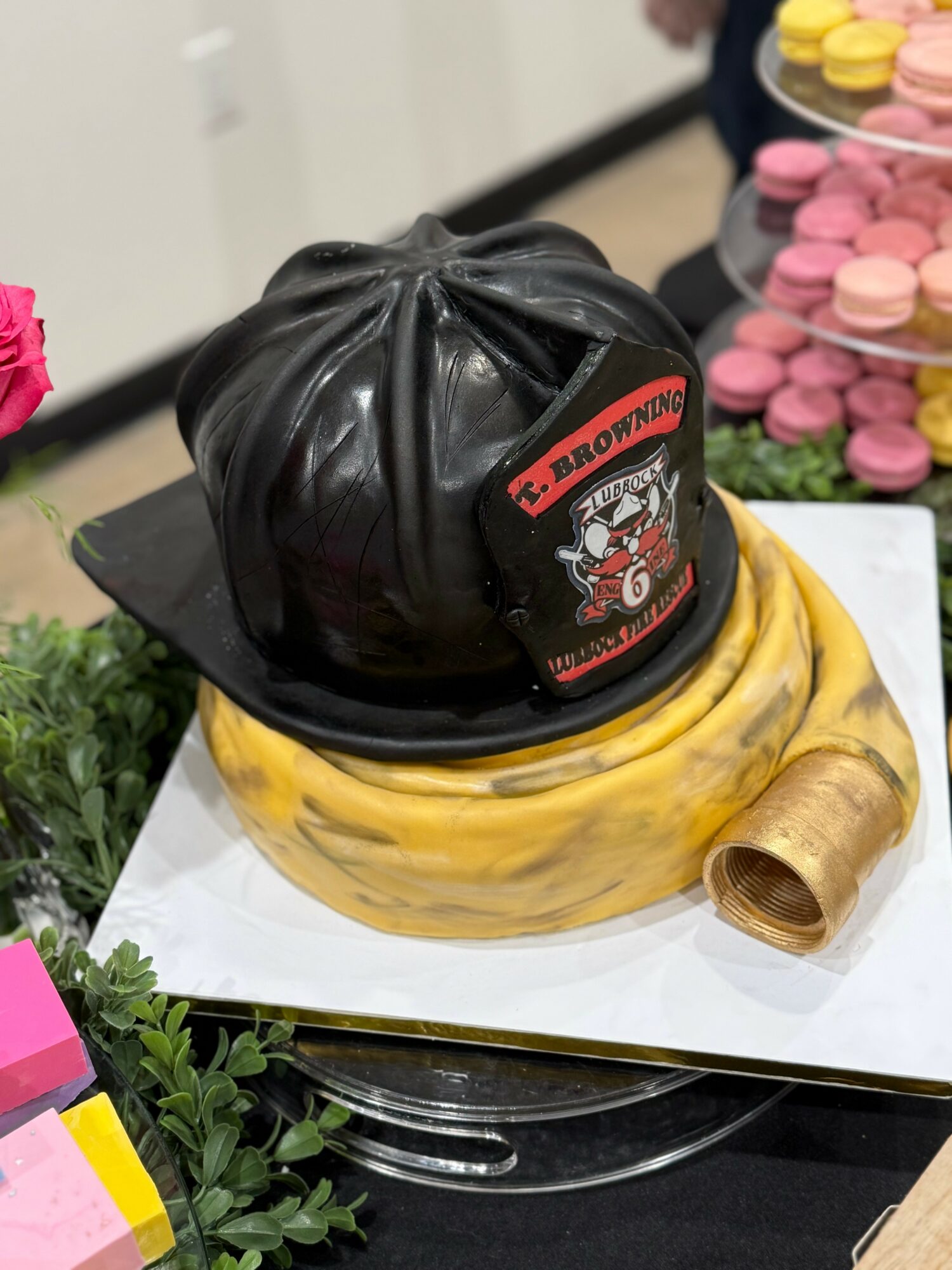 A cake decorated with a black helmet and a banana, placed on a white surface with pink and yellow macarons in the background.