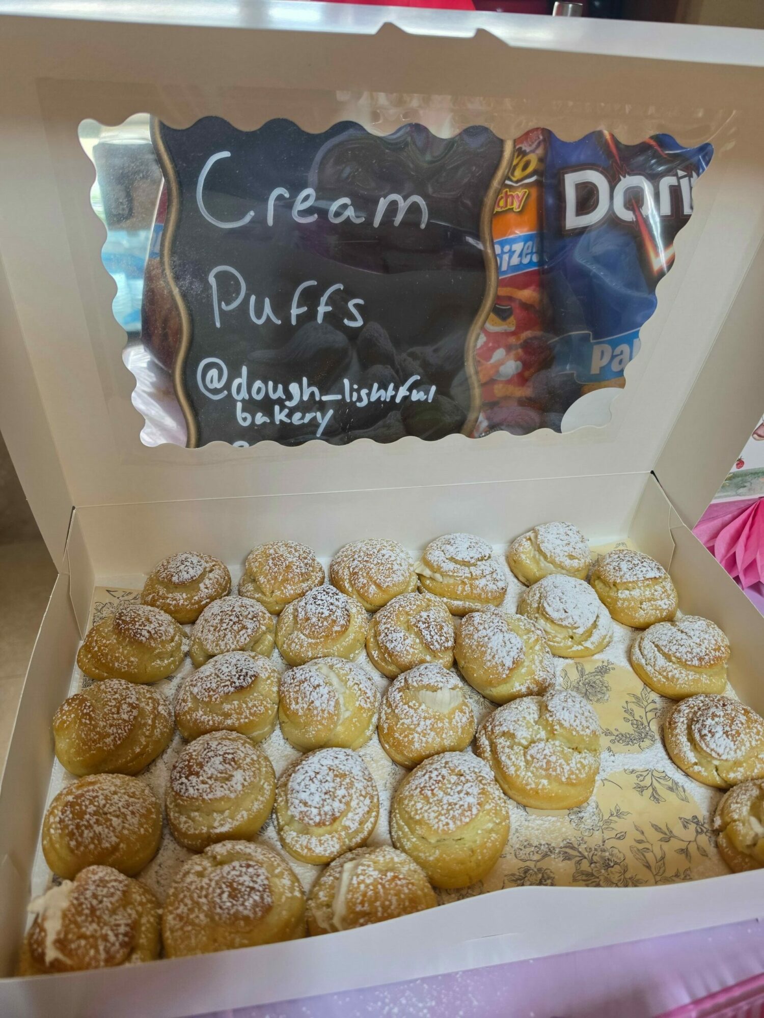 Box of cream puffs dusted with powdered sugar inside a pink-lined box.