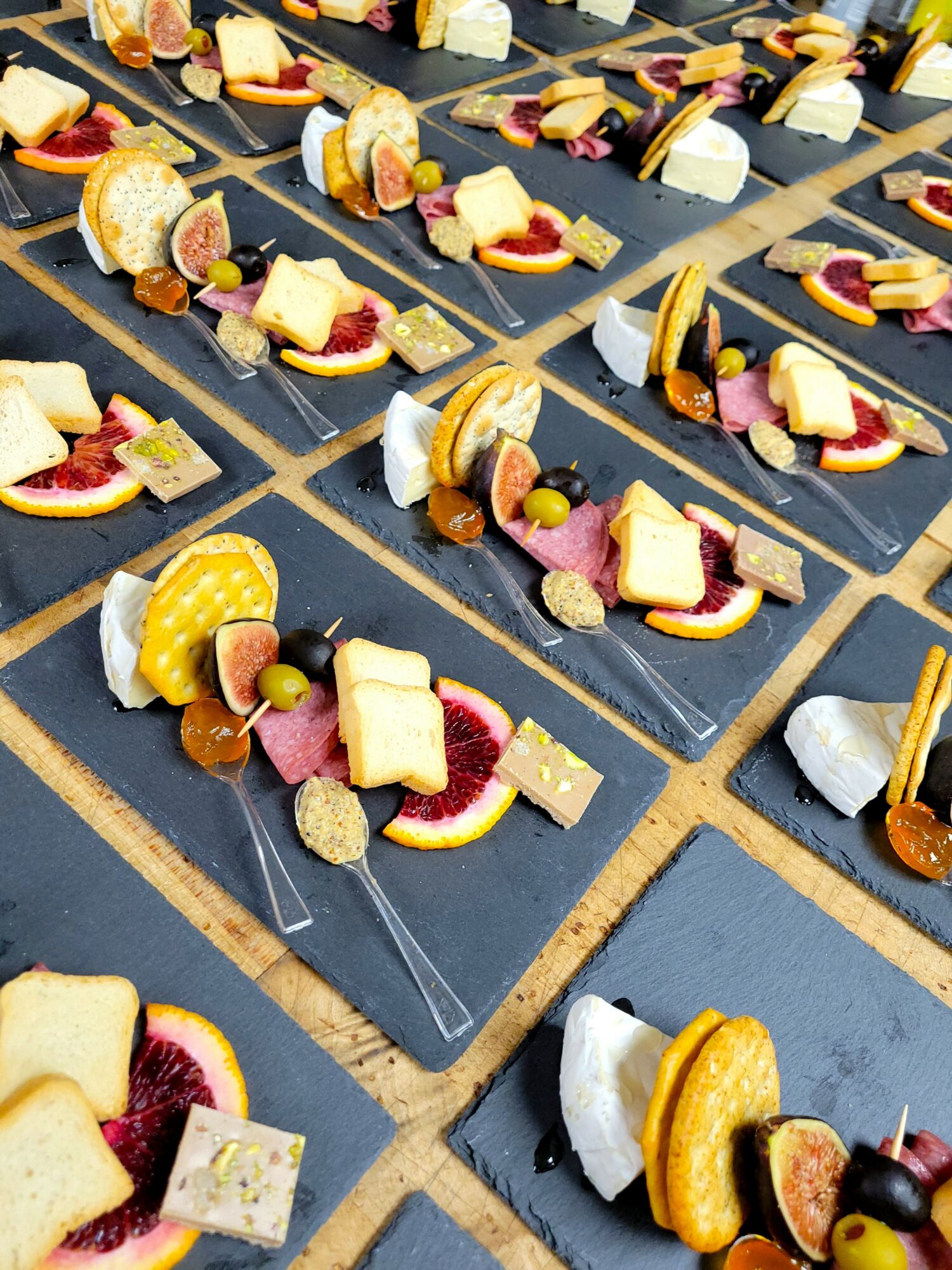 Multiple black rectangular plates with assorted desserts arranged in rows, including cookies, fruit, and cream, on a gray surface.