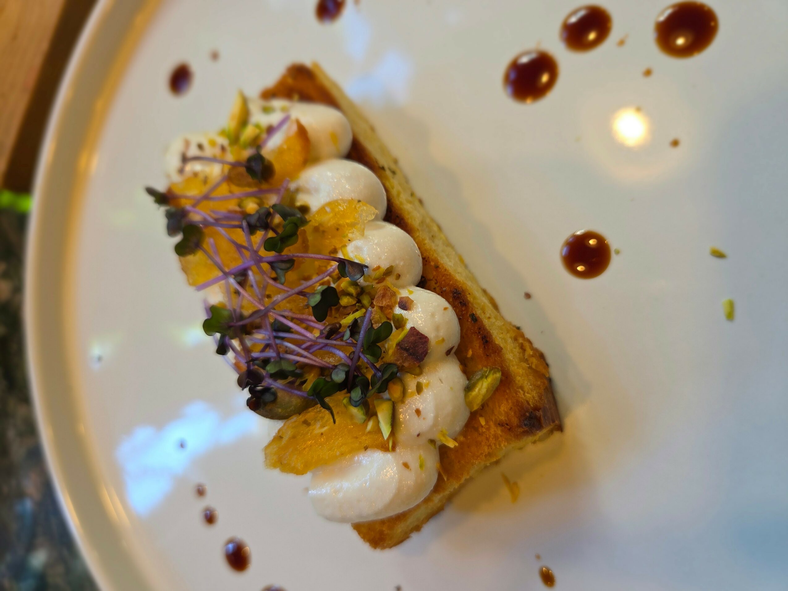 A plated dessert with cream, fruit, edible flowers, and sauce dots on a white plate.