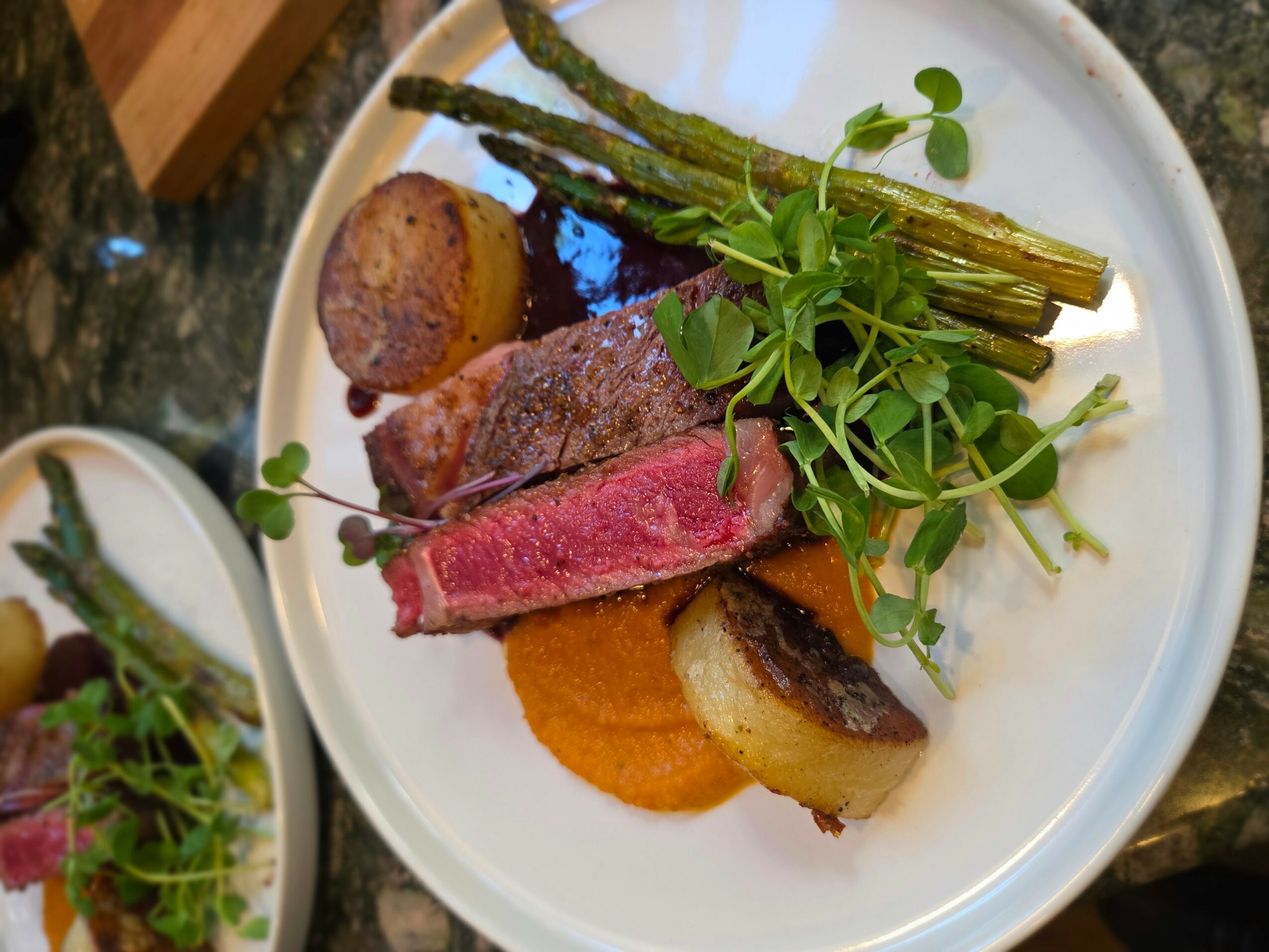 Plate with cooked meat, grilled asparagus, greens, and roasted vegetables, arranged on a white dish.