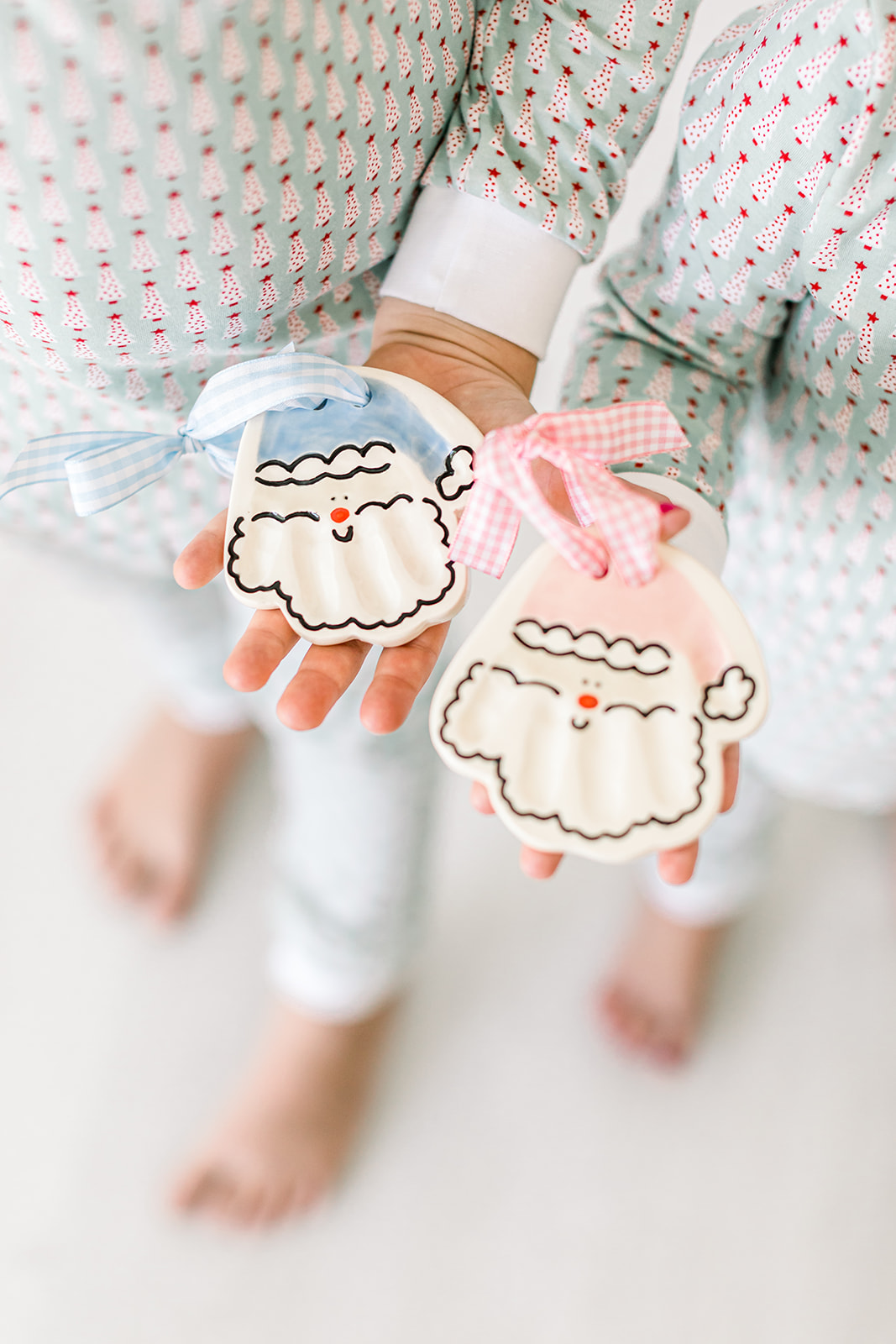 Two children hold plush cloud-shaped toys with pink and blue bows, wearing pajamas with small polka dots, standing barefoot.