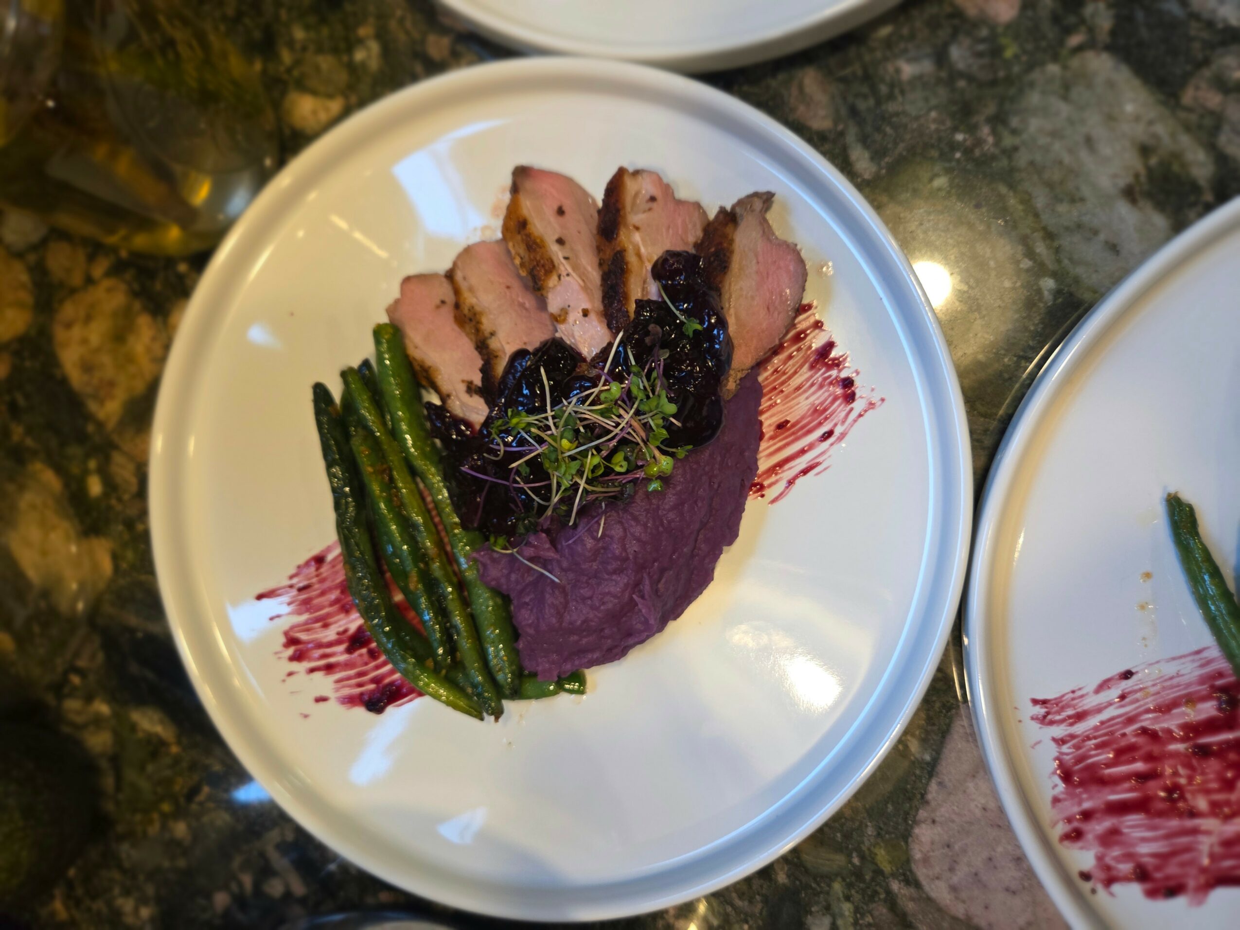 Sliced cooked meat with green beans and purple sauce on a white plate.