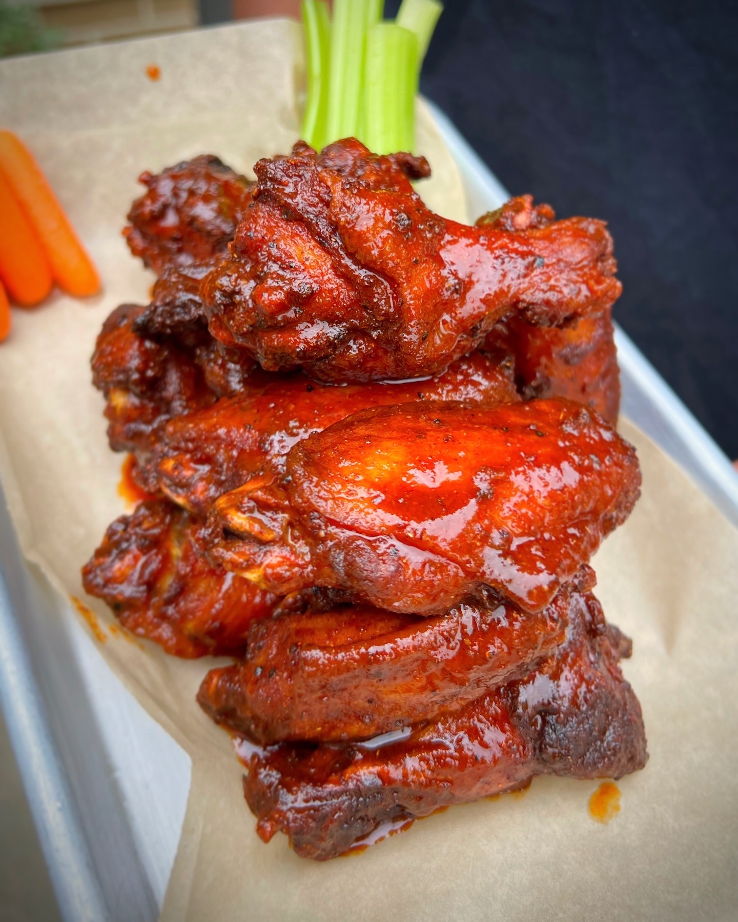 Stack of glazed chicken wings with celery sticks in the background on a tray.