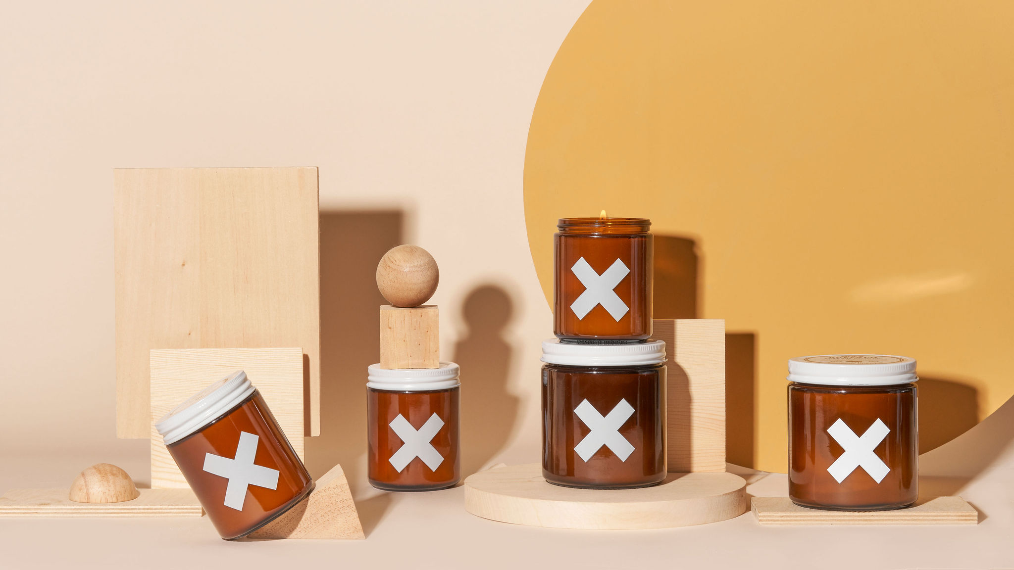 Six brown medicine bottles with white crosses, some stacked, on a beige and yellow background with geometric shapes.