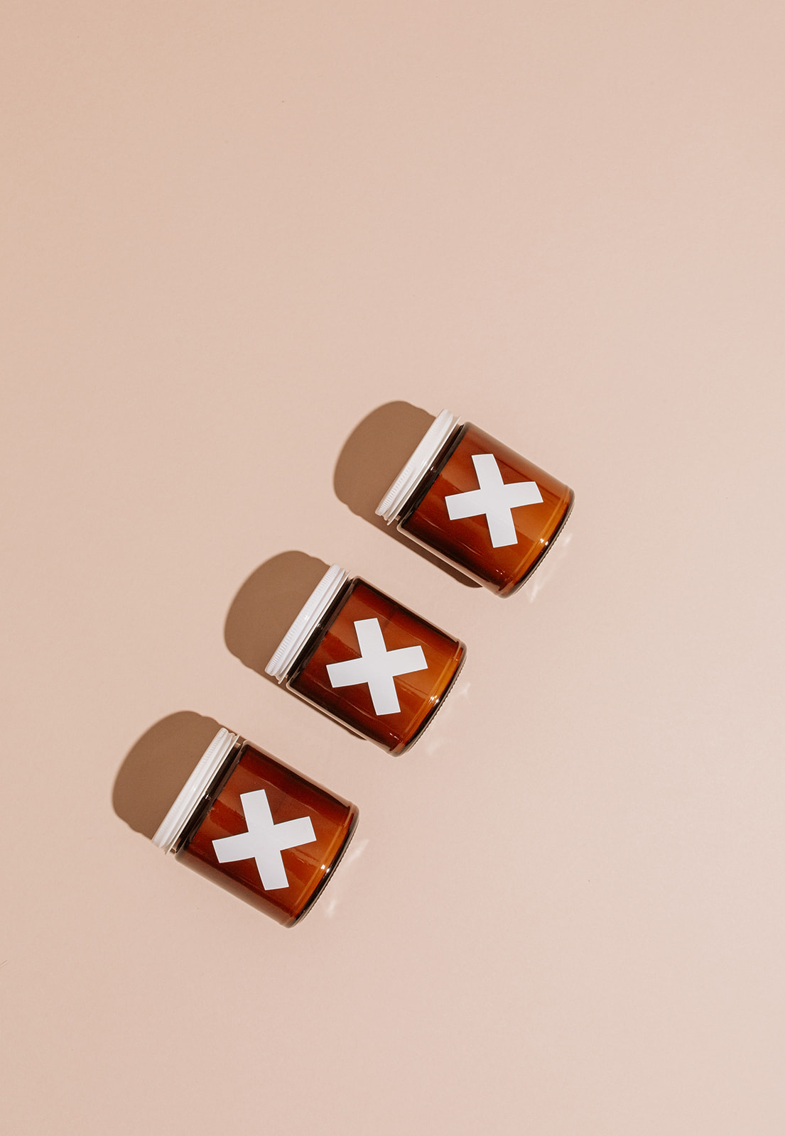 Three pill bottles with white crosses on red labels arranged diagonally on a light background.