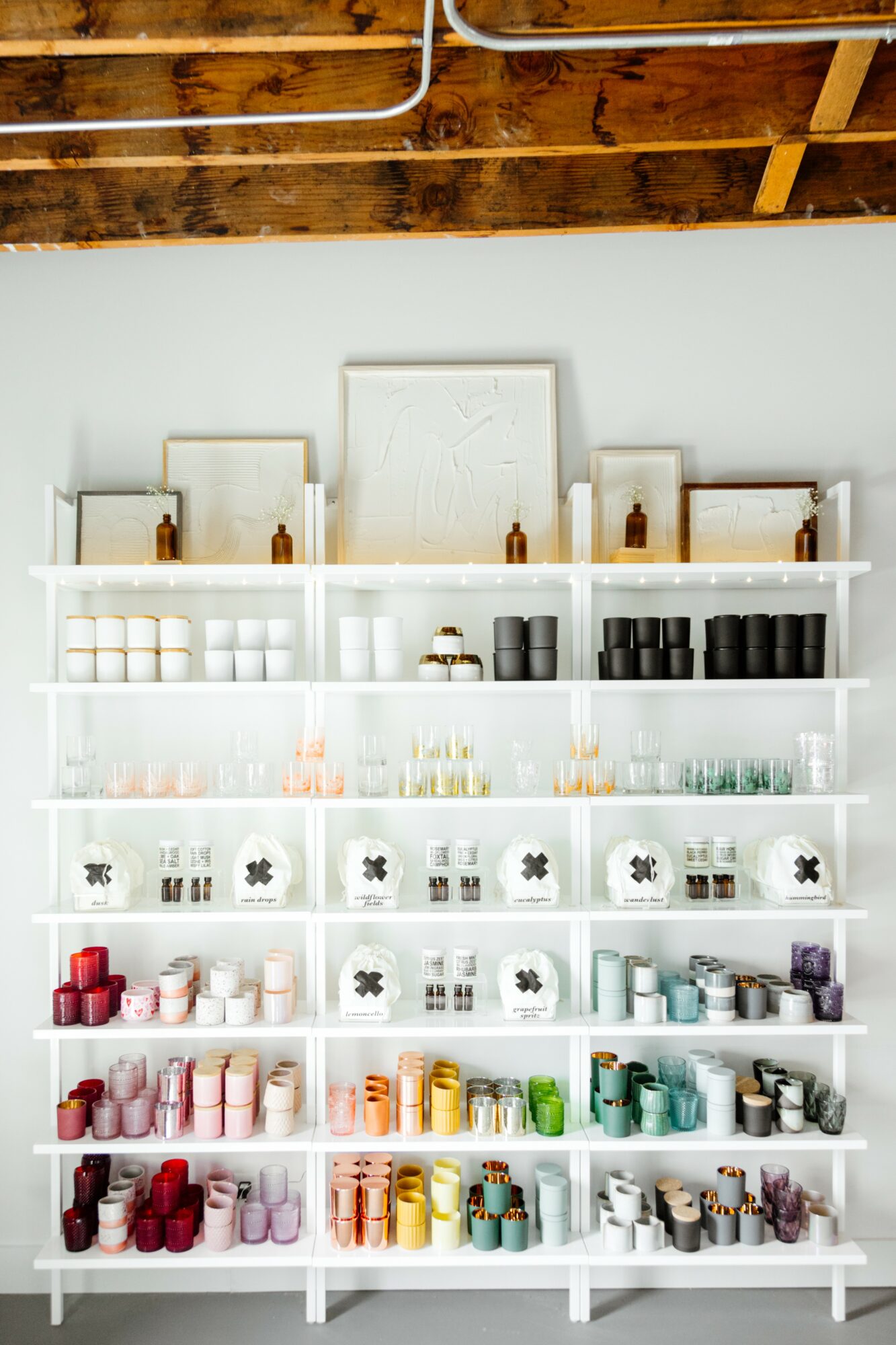 White shelves filled with various bottles, jars, and containers against a white wall, ceiling with exposed wooden beams.