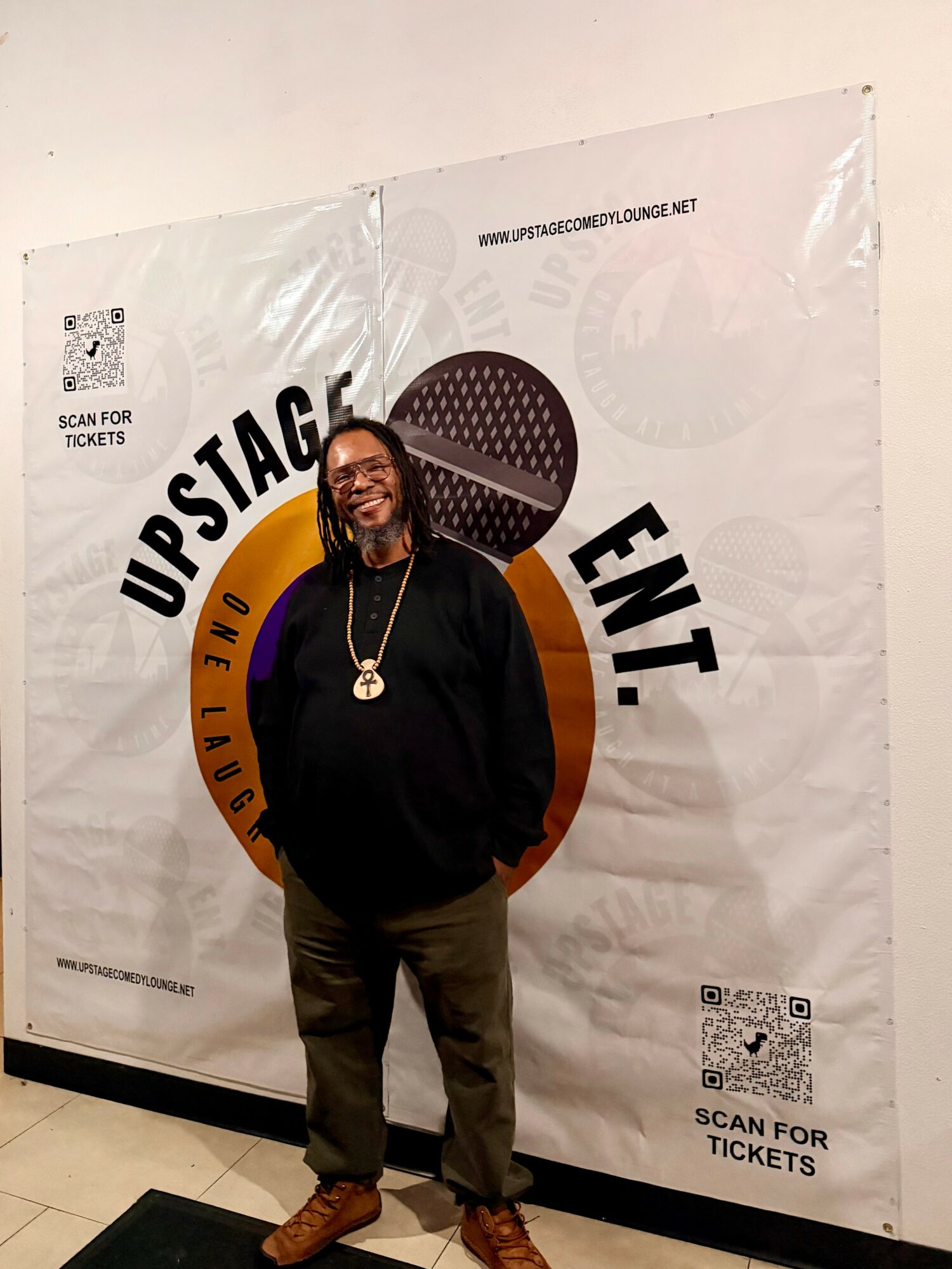 Person with glasses and a necklace standing in front of a large poster with text and graphics.
