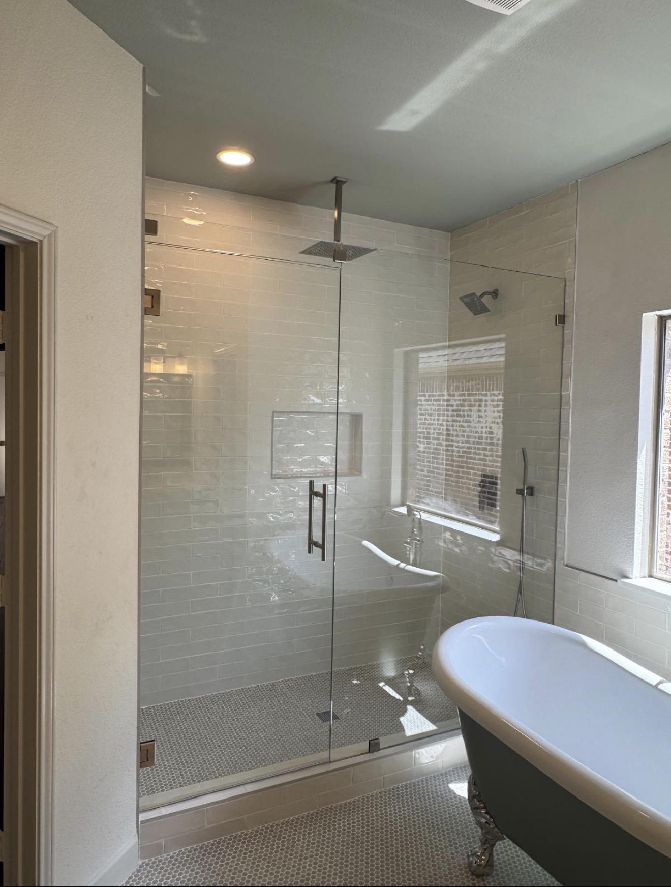 Bathroom with glass shower enclosure, bathtub, window, and ceiling light, viewed from doorway.