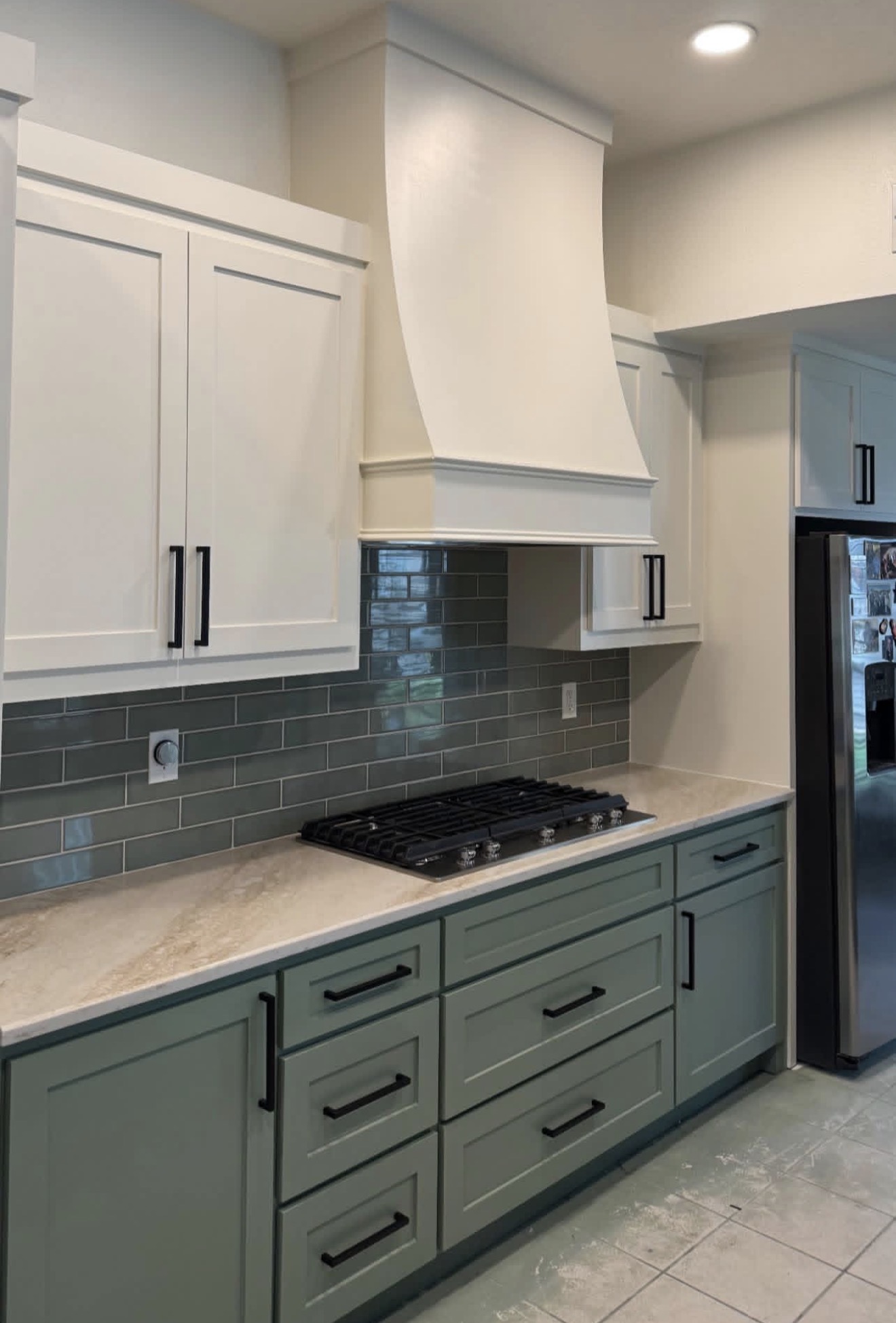 Kitchen with white upper cabinets, green lower cabinets, gray backsplash, and a stove beneath a white range hood.
