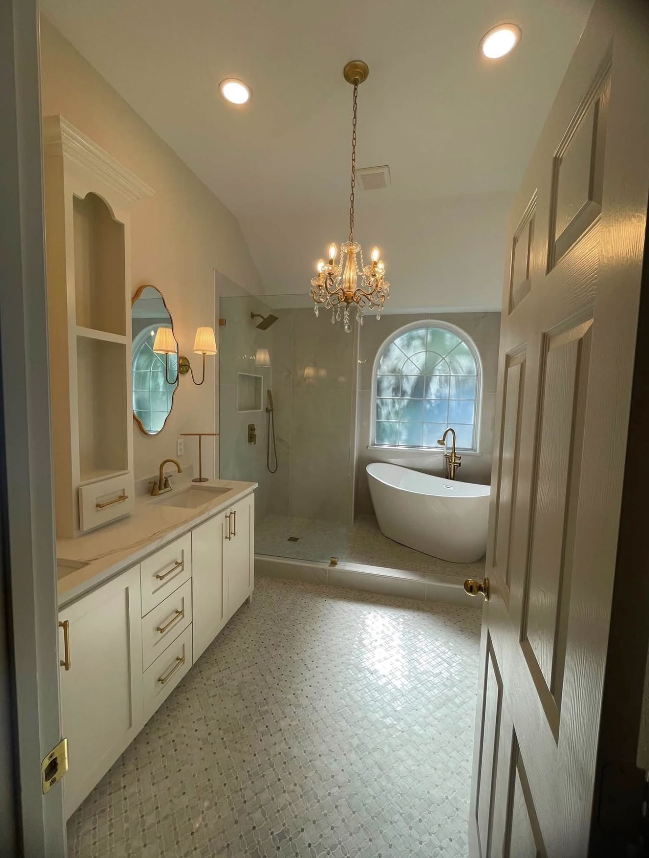 Bathroom with a bathtub near a window, chandelier, and a vanity with a mirror, viewed from the doorway.