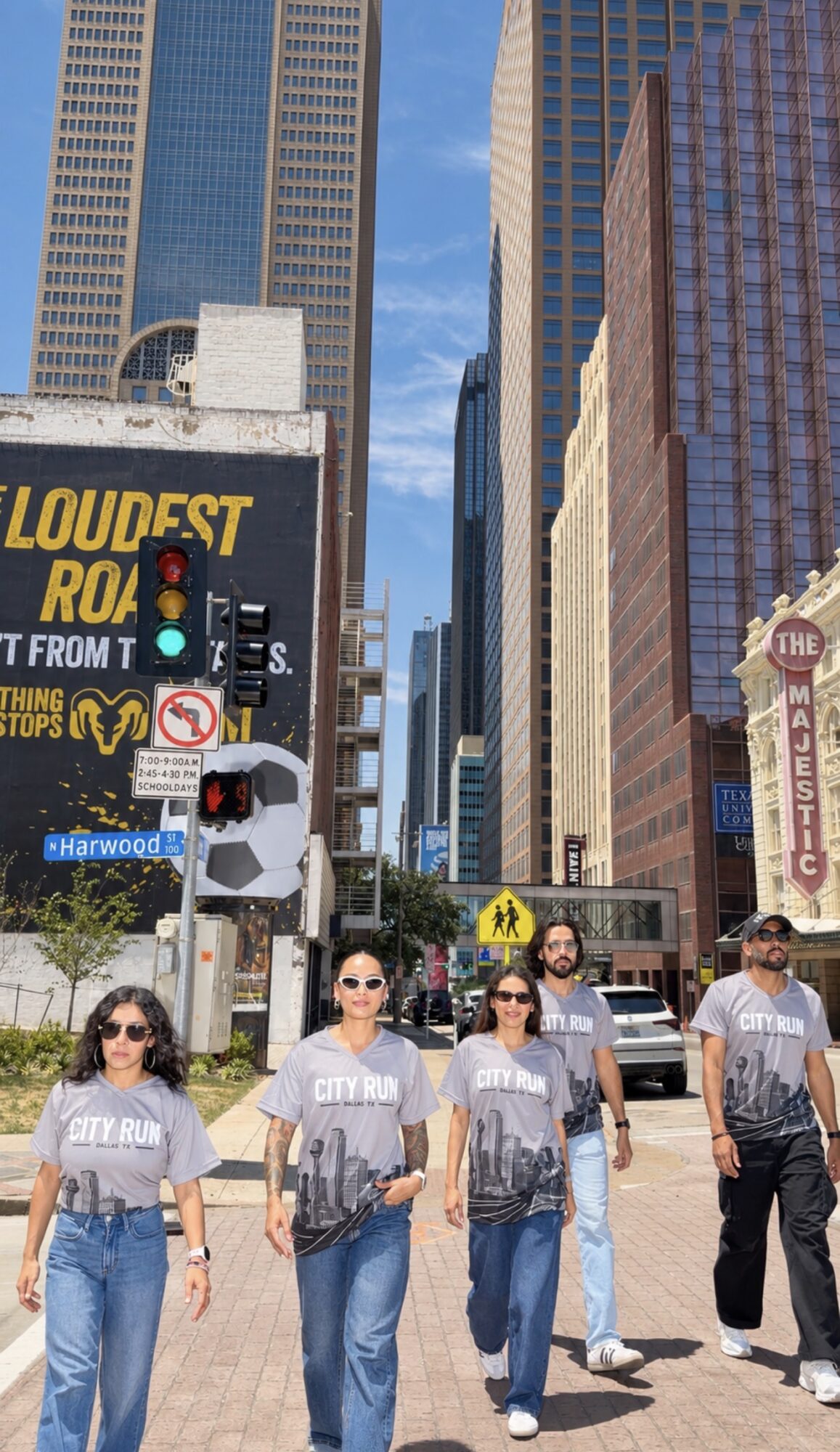 Group of four people walking in a city street with tall buildings and billboards, sunny weather.