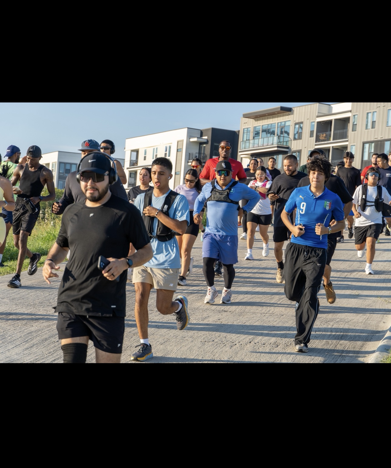 Group of people running outdoors near modern buildings on a sunny day.